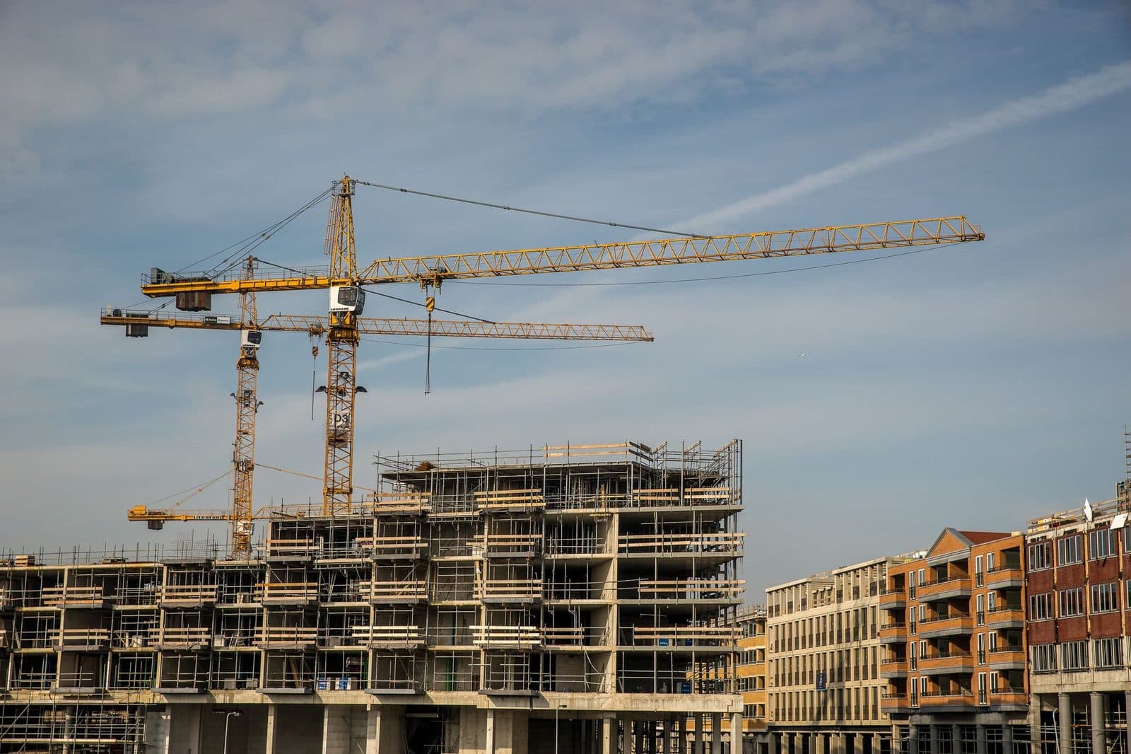 Chantier de construction d'immeubles en béton avec échafaudages et deux grues jaunes sous un ciel bleu