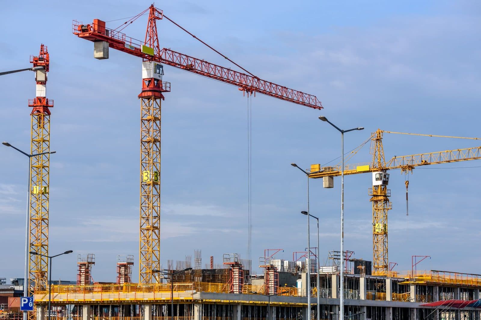 Grues rouges et jaunes au-dessus d'un chantier de construction d'immeubles en béton sous un ciel bleu