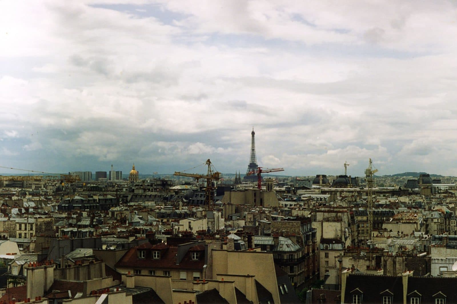 Vue sur les toits de Paris avec grues de chantier et tour Eiffel à l'horizon sous un ciel nuageux