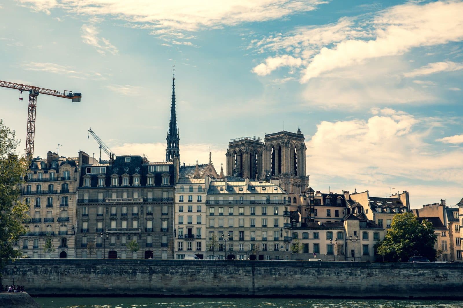 Grues de chantier au-dessus des immeubles haussmanniens et de Notre-Dame de Paris, au bord de la Seine