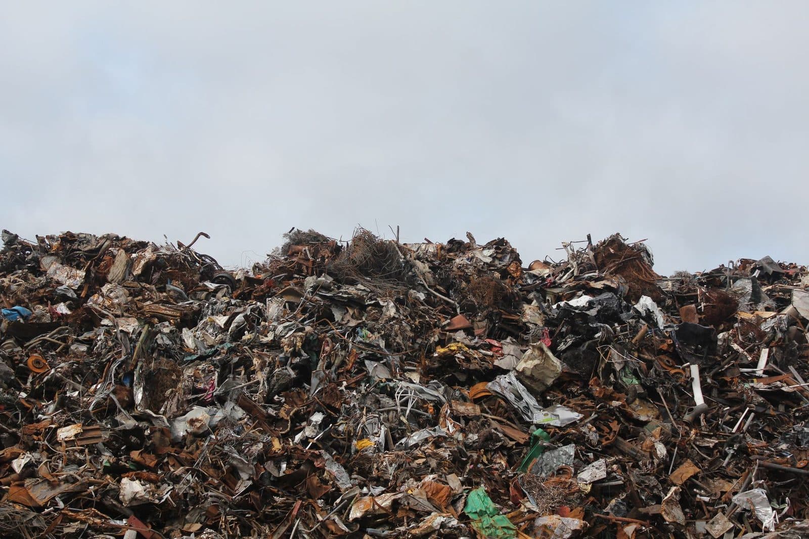 Vaste amas de déchets et débris mêlant métal, bois et plastique sur un site de décharge, sous un ciel gris