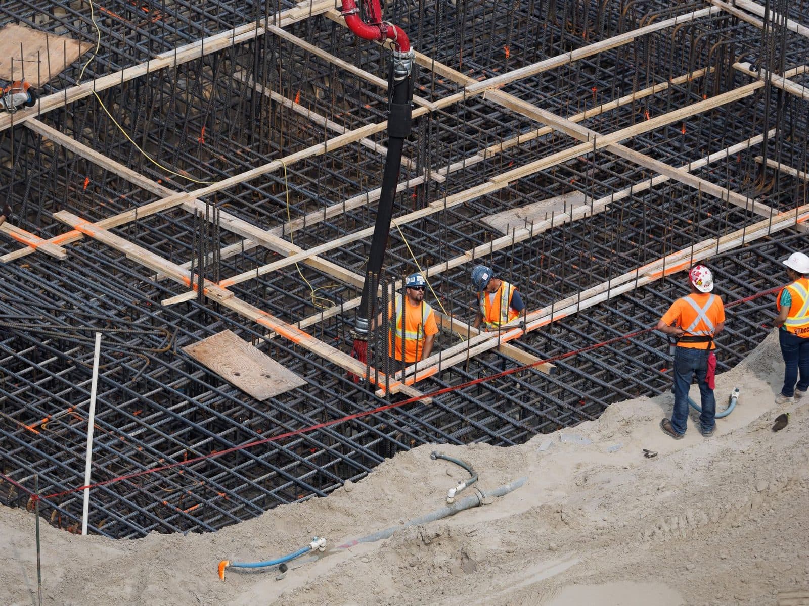 Ouvriers en gilets orange sur un chantier de construction, ferraillage de fondations et pompe à béton