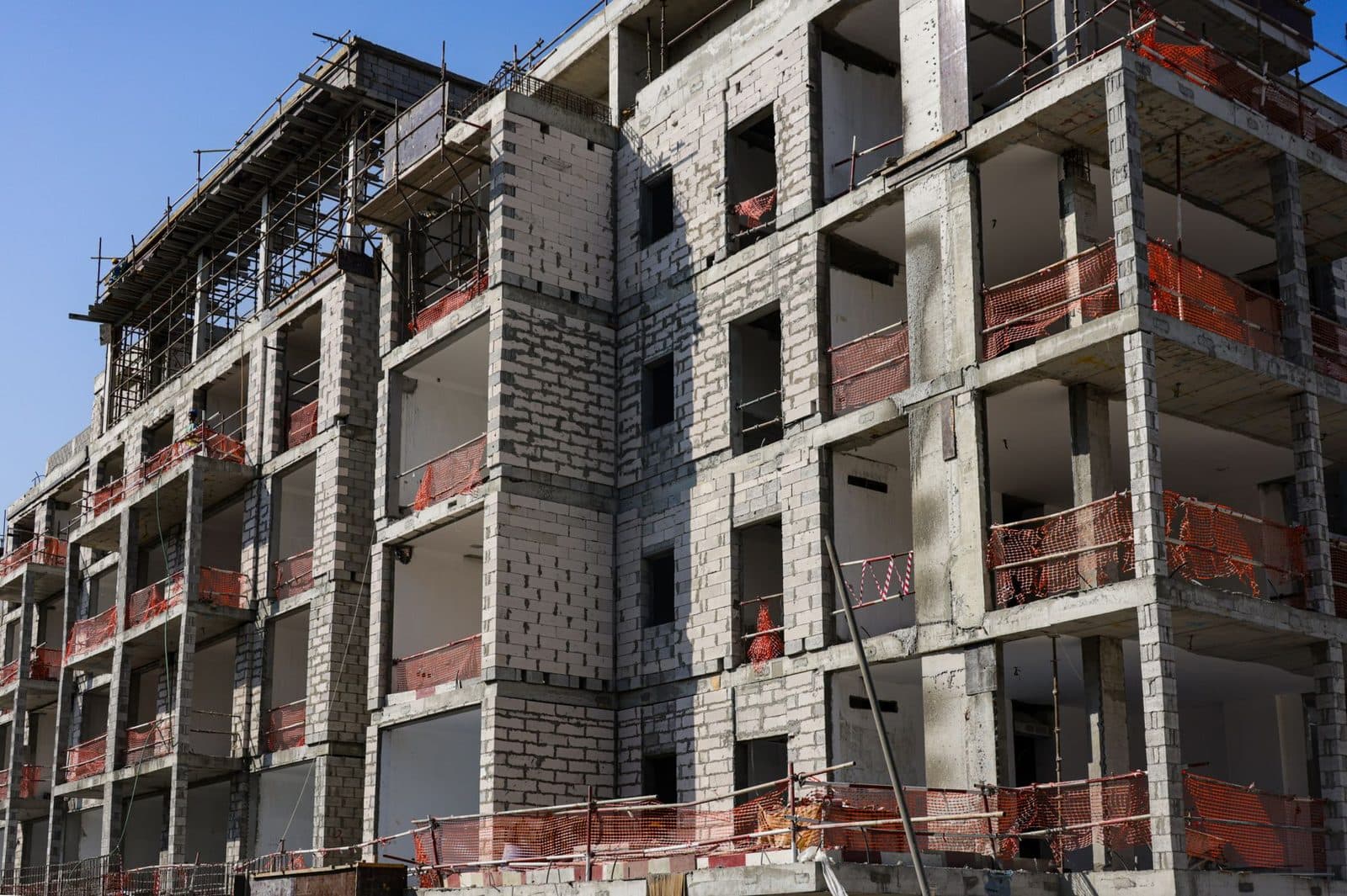 Immeuble résidentiel en construction, structure béton avec échafaudages et filets de sécurité orange