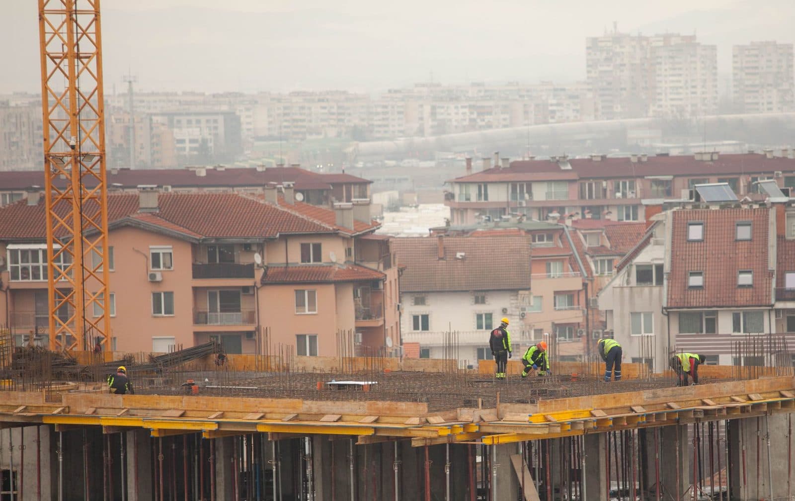 Ouvriers sur la dalle en coffrage d'un immeuble en construction avec grue jaune, devant des logements urbains