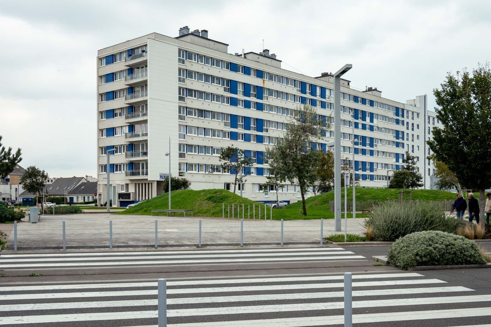 Immeuble collectif de logements à façade blanche et bleue, vu depuis un passage piéton