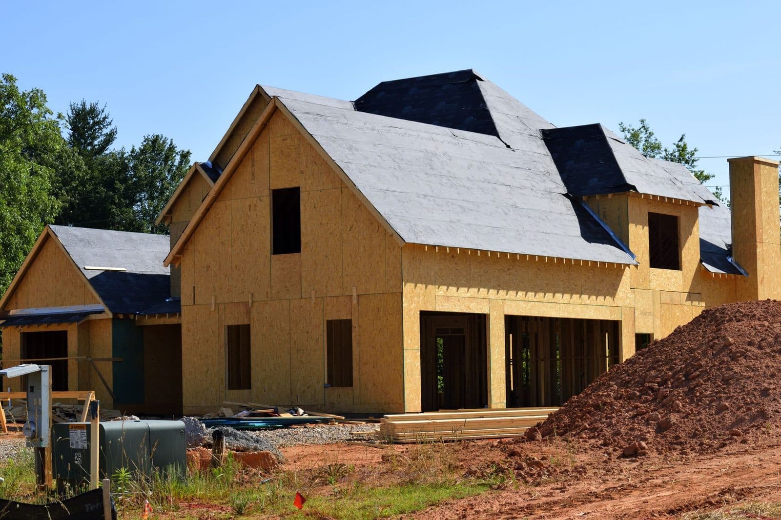 Maison en construction inachevée, ossature bois et panneaux OSB apparents, chantier à l'arrêt avec terre remuée