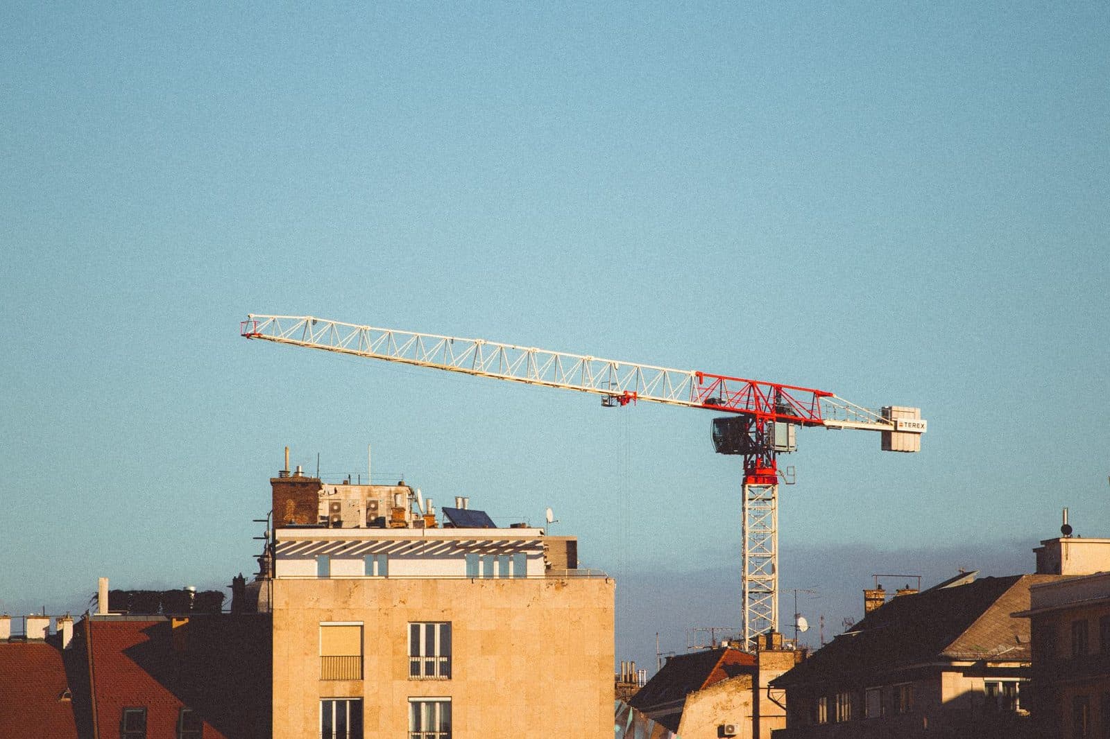 Grue de chantier rouge et blanche dressée au-dessus des toits d'immeubles urbains sous un ciel bleu