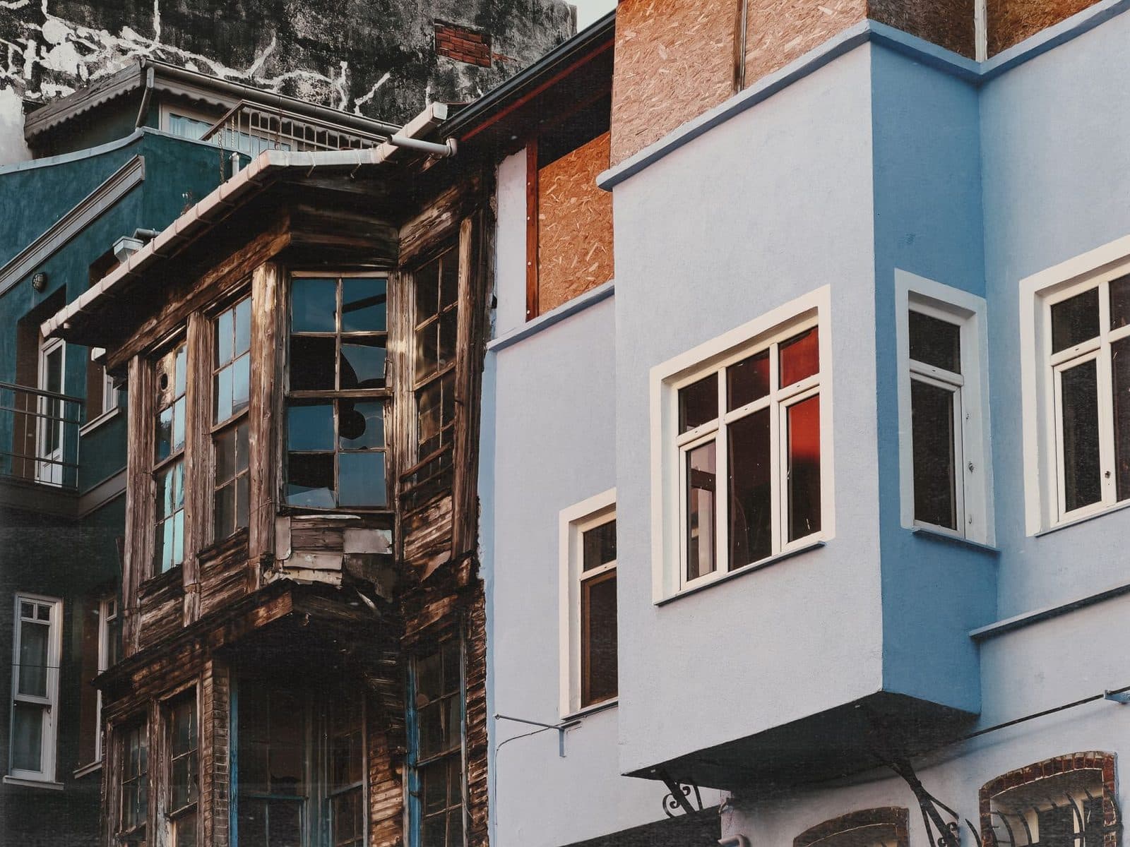 Façades d'immeubles anciens : bâtiment en bois dégradé entre deux immeubles rénovés aux murs bleus