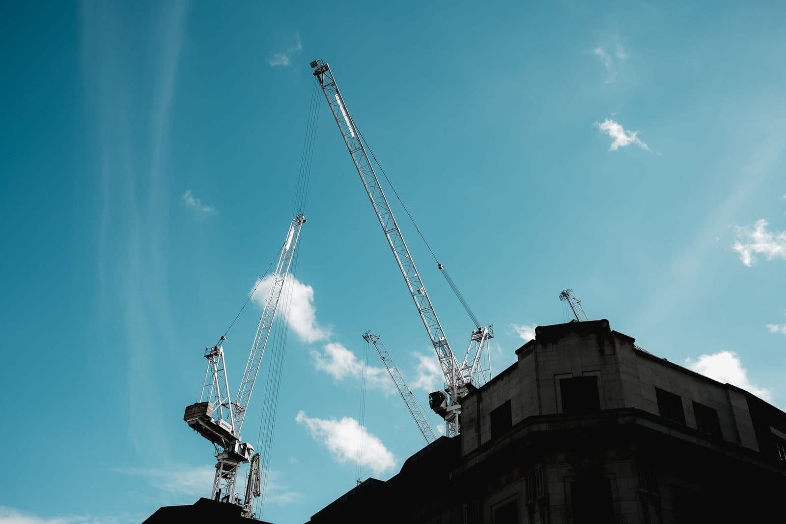Deux grues de chantier au-dessus d'un immeuble en pierre, sous un ciel bleu