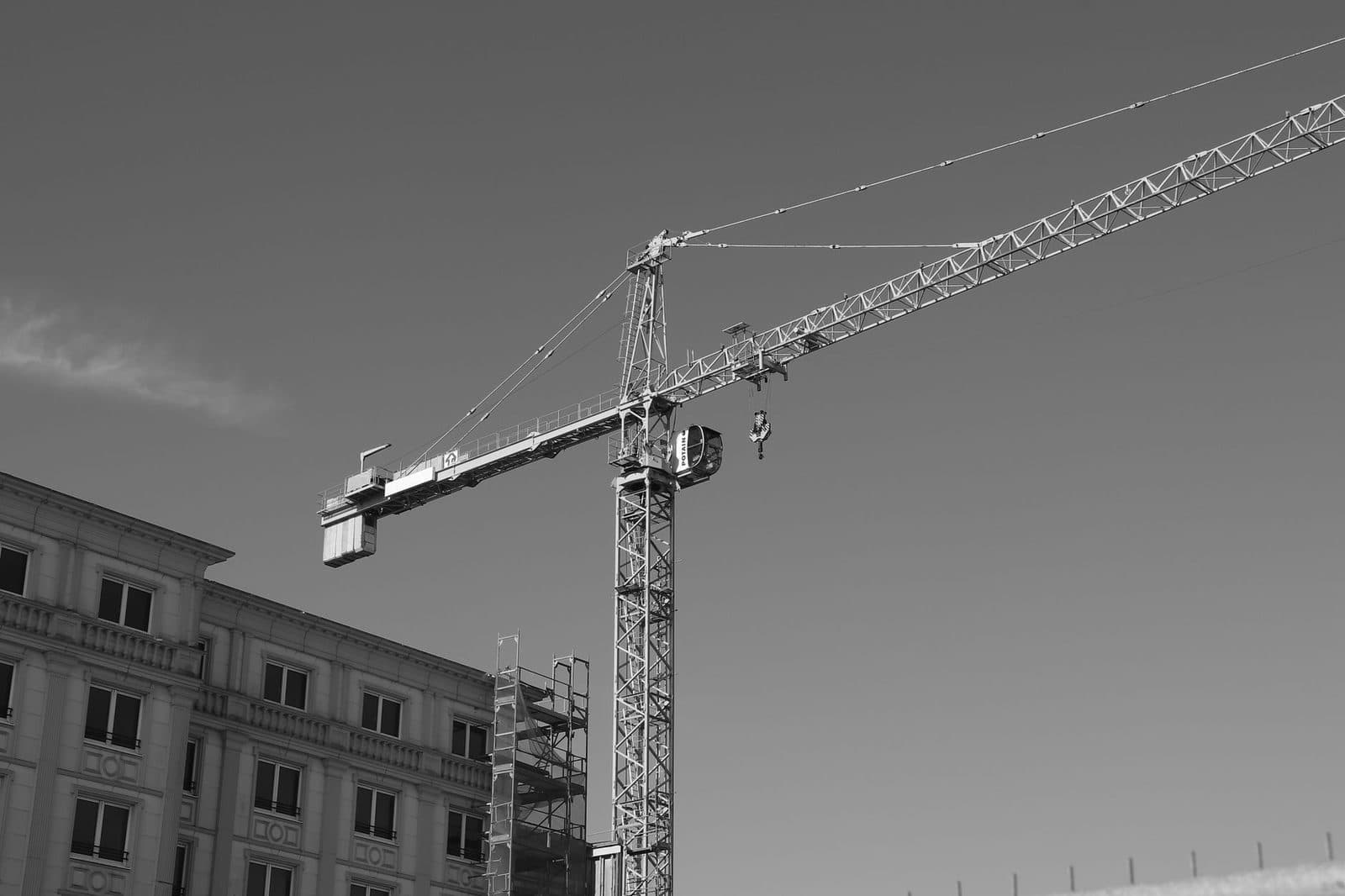 Grue à tour sur un chantier de construction, à côté d'un immeuble en pierre, photo en noir et blanc