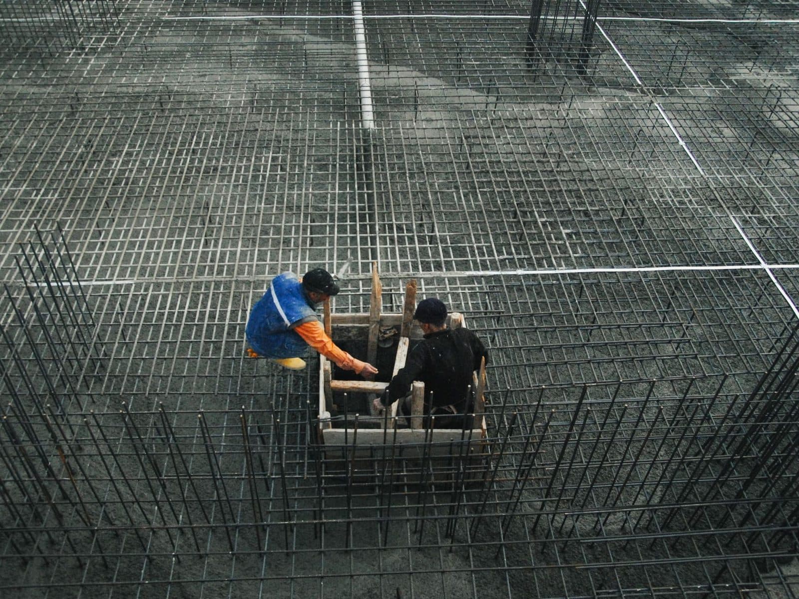 Deux ouvriers travaillant sur un vaste ferraillage d'armatures métalliques avant coulage du béton sur un chantier