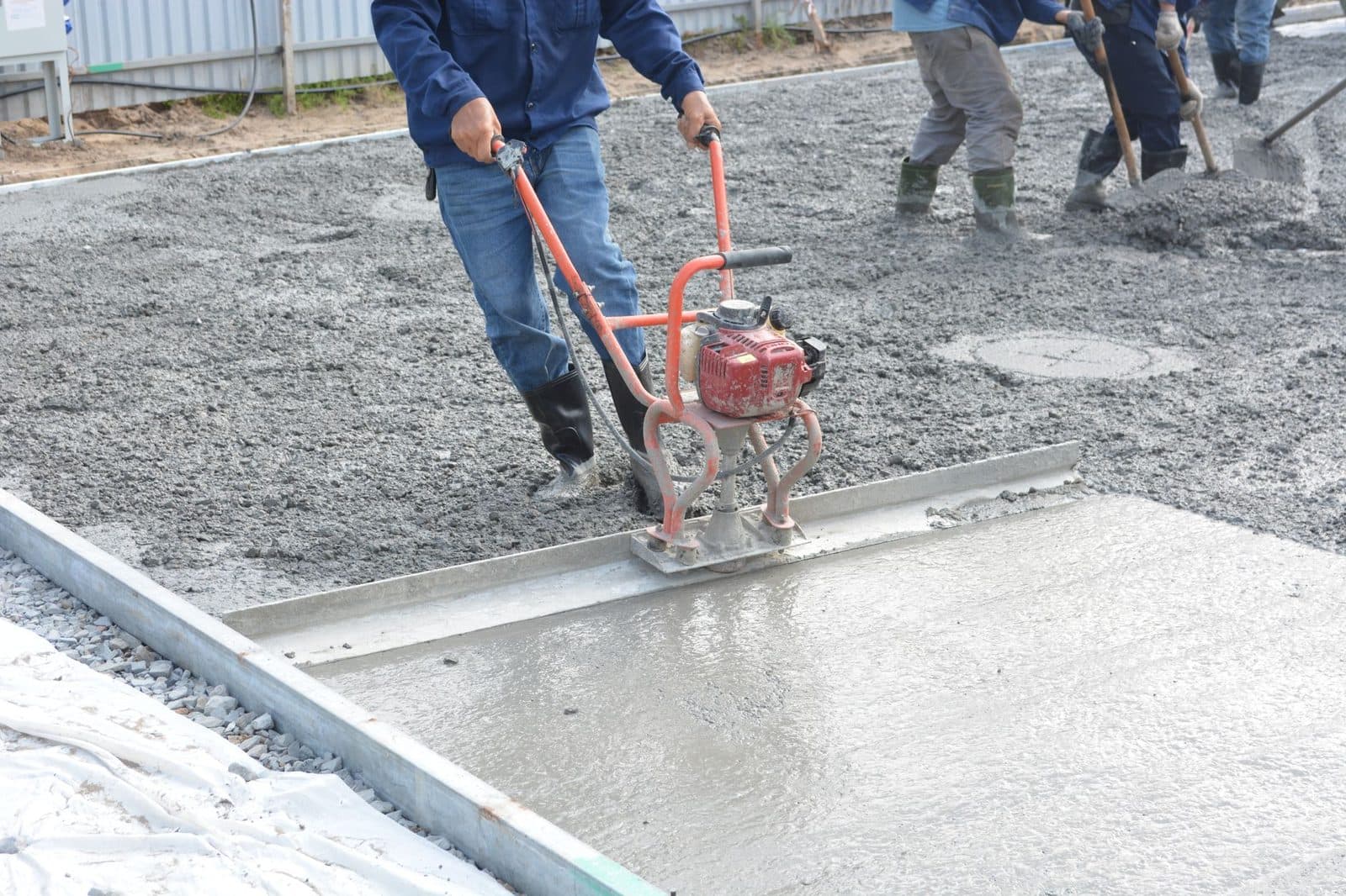 Ouvriers coulant et lissant une dalle de béton frais à la règle vibrante sur un chantier de construction