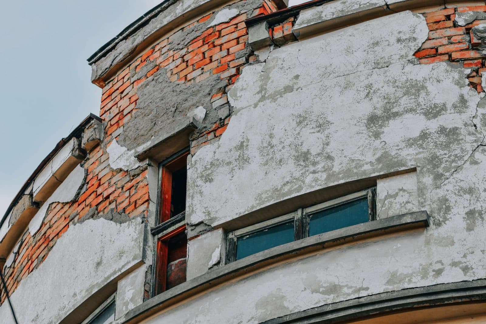 Façade dégradée d'un immeuble ancien, enduit écaillé laissant apparaître les briques et fenêtres vétustes
