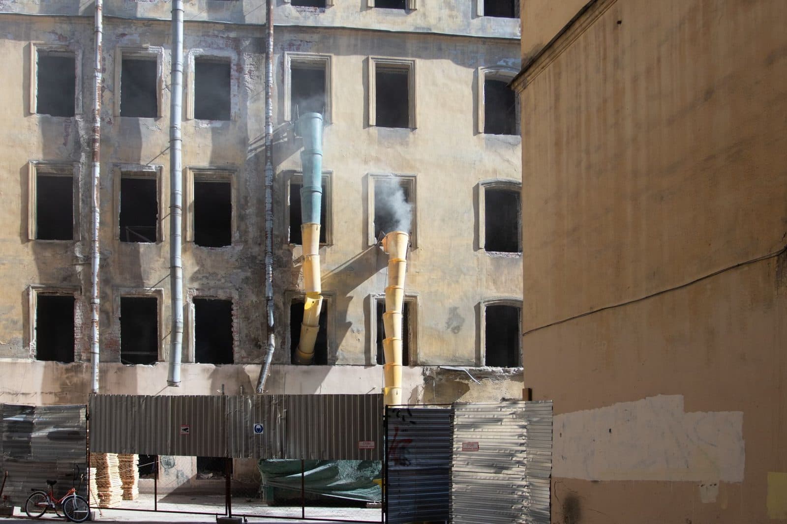 Immeuble ancien en rénovation avec façade dégradée, goulottes à gravats et palissades de chantier