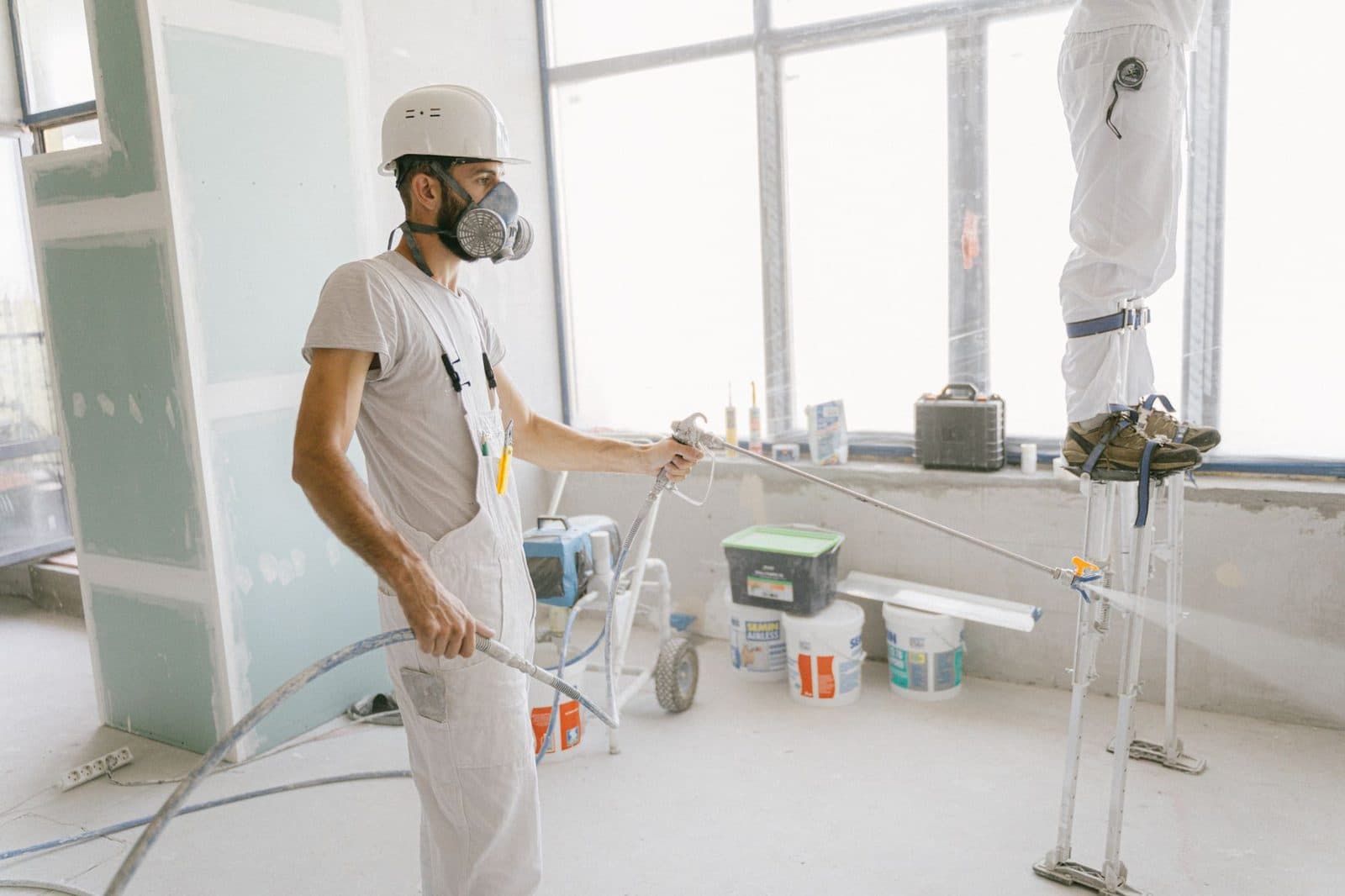 Ouvrier en combinaison blanche et masque appliquant un enduit au pistolet dans un logement en rénovation