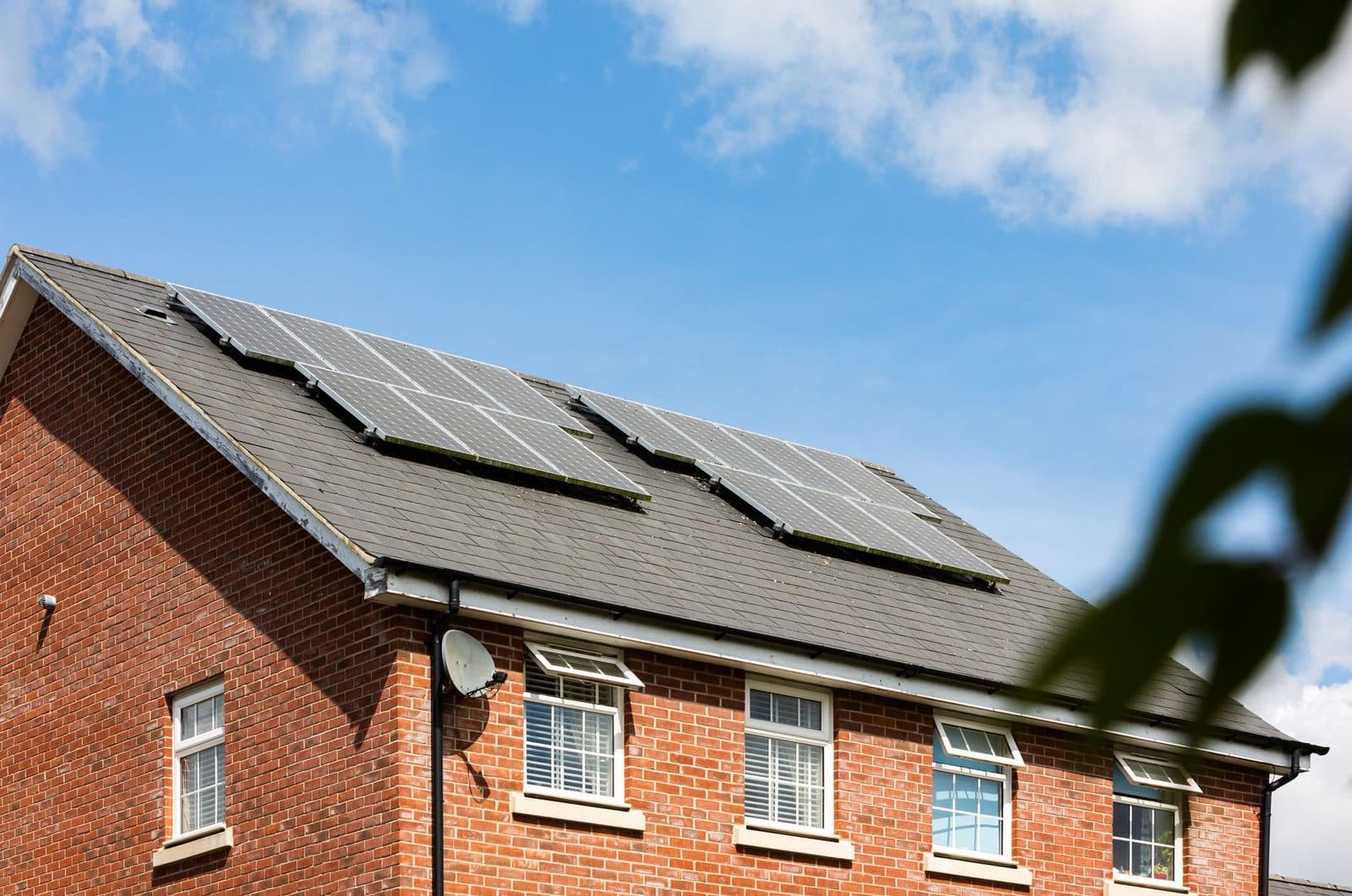 Panneaux solaires installés sur le toit en ardoise d'une maison en briques rouges sous un ciel bleu