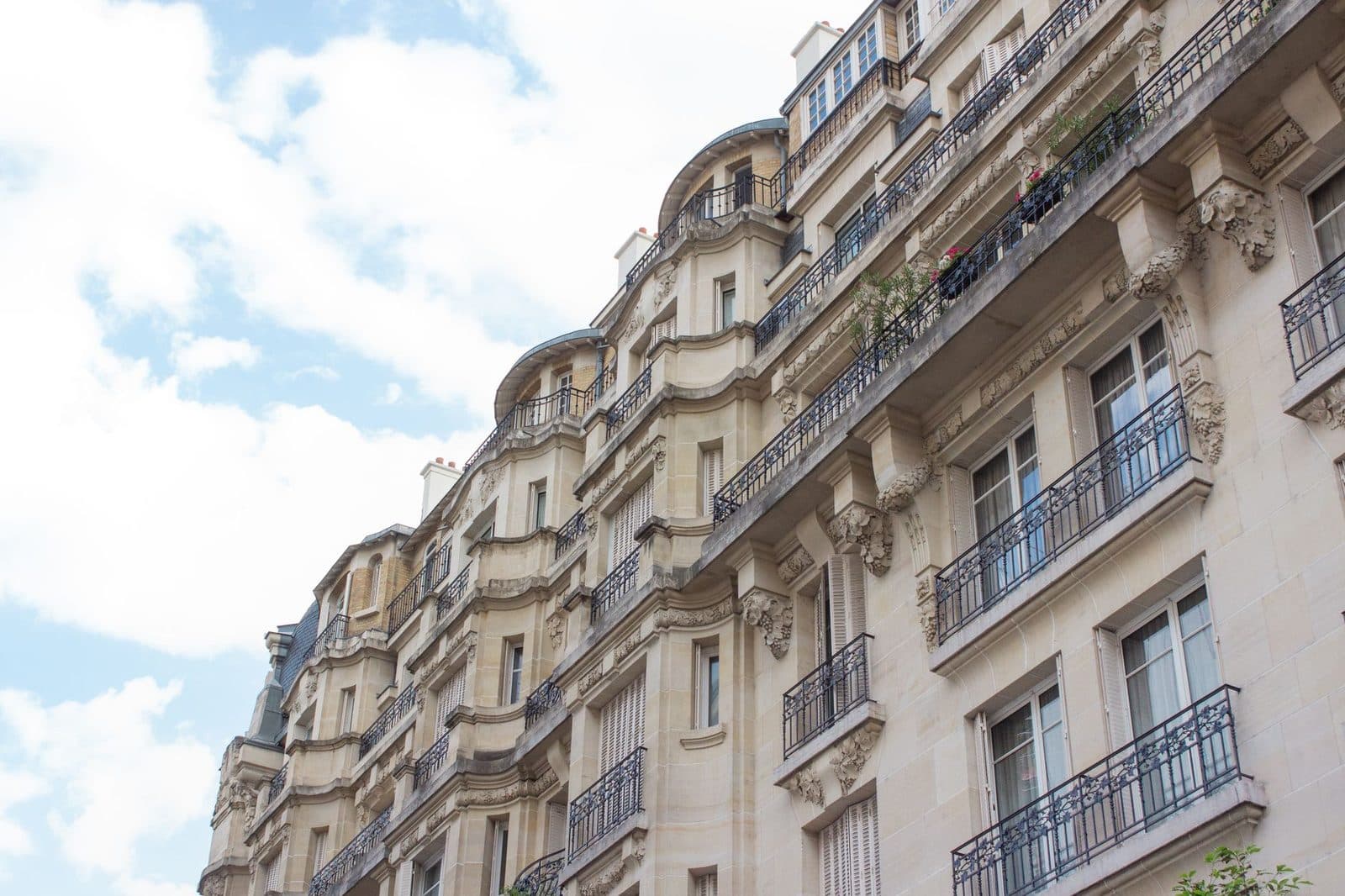 Façade d'immeubles haussmanniens en pierre avec balcons en fer forgé et fenêtres, vue en contre-plongée