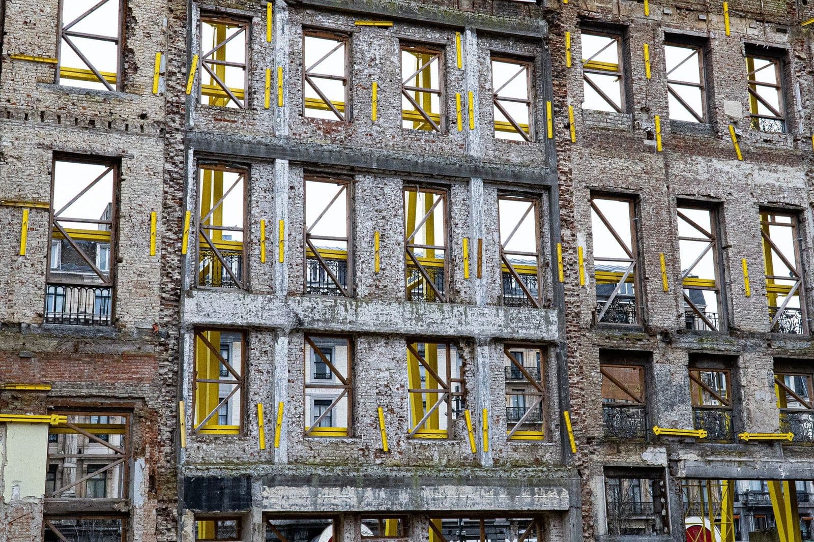 Façade d'immeuble haussmannien conservée et étayée par des poutrelles jaunes et des croix de bois sur un chantier