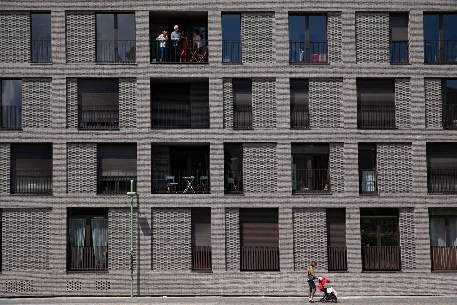 Façade en brique d'un immeuble de logements neufs, femme avec poussette marchant sur le trottoir