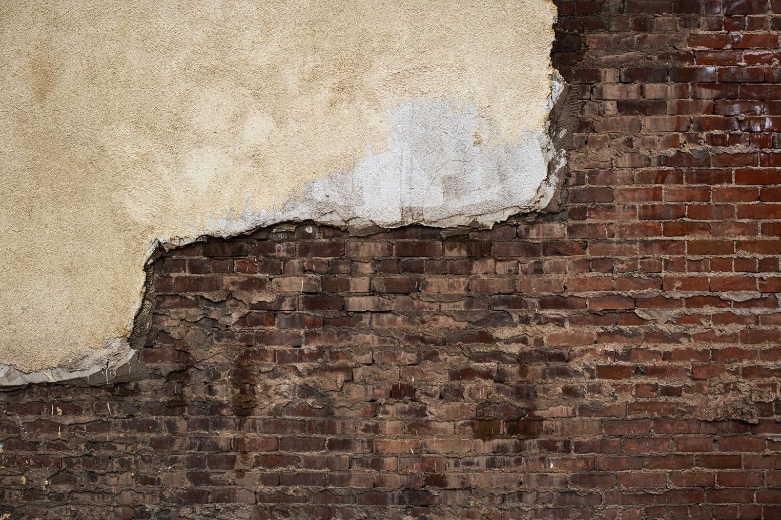 Façade dégradée : enduit décollé laissant apparaître un mur de briques anciennes abîmées