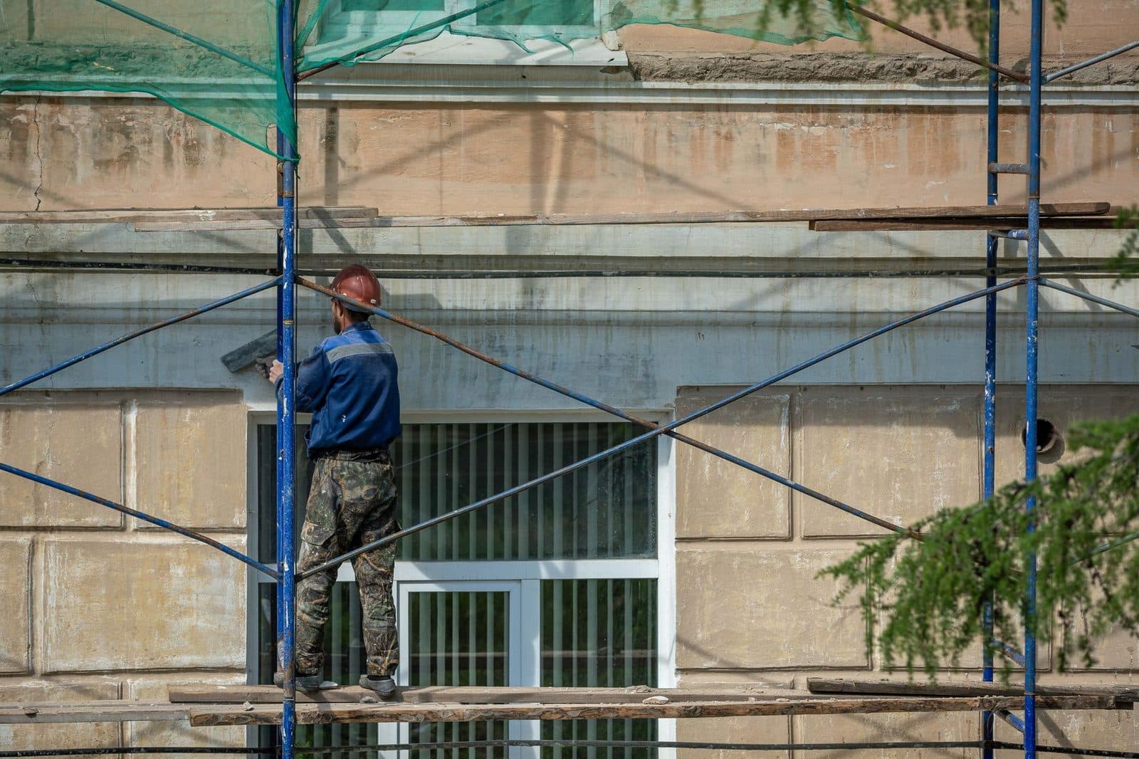 Ouvrier casqué sur un échafaudage enduisant la façade d'un bâtiment en rénovation