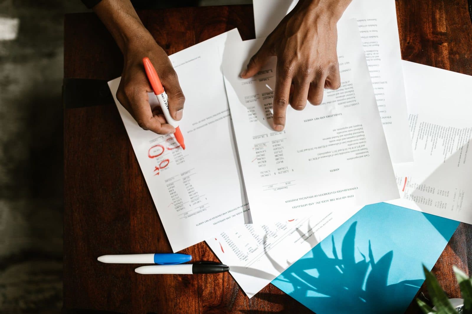 Mains annotant au marqueur rouge des documents administratifs étalés sur une table en bois