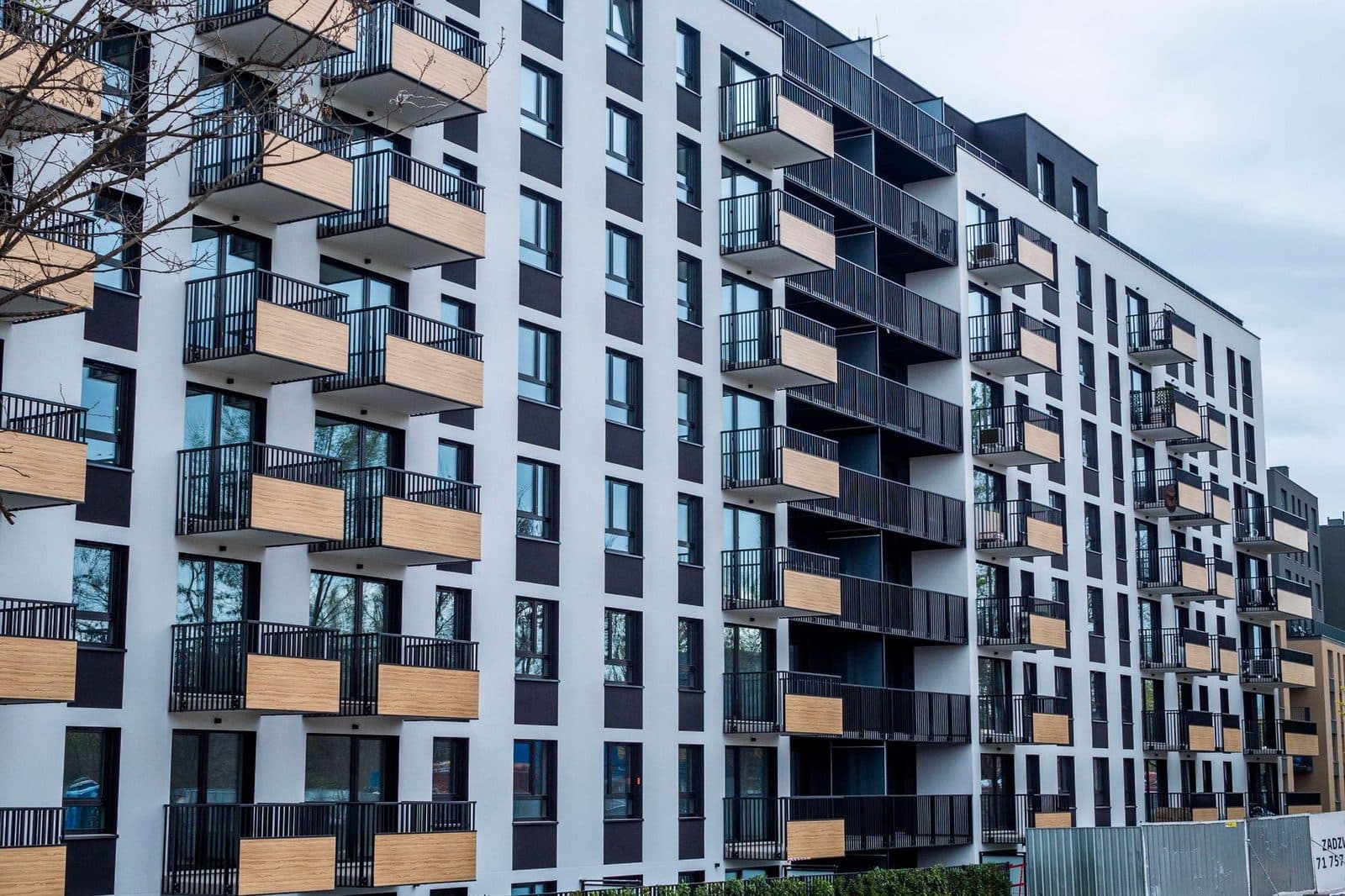Façade d'un immeuble résidentiel neuf avec balcons en bois et palissade de chantier au pied du bâtiment