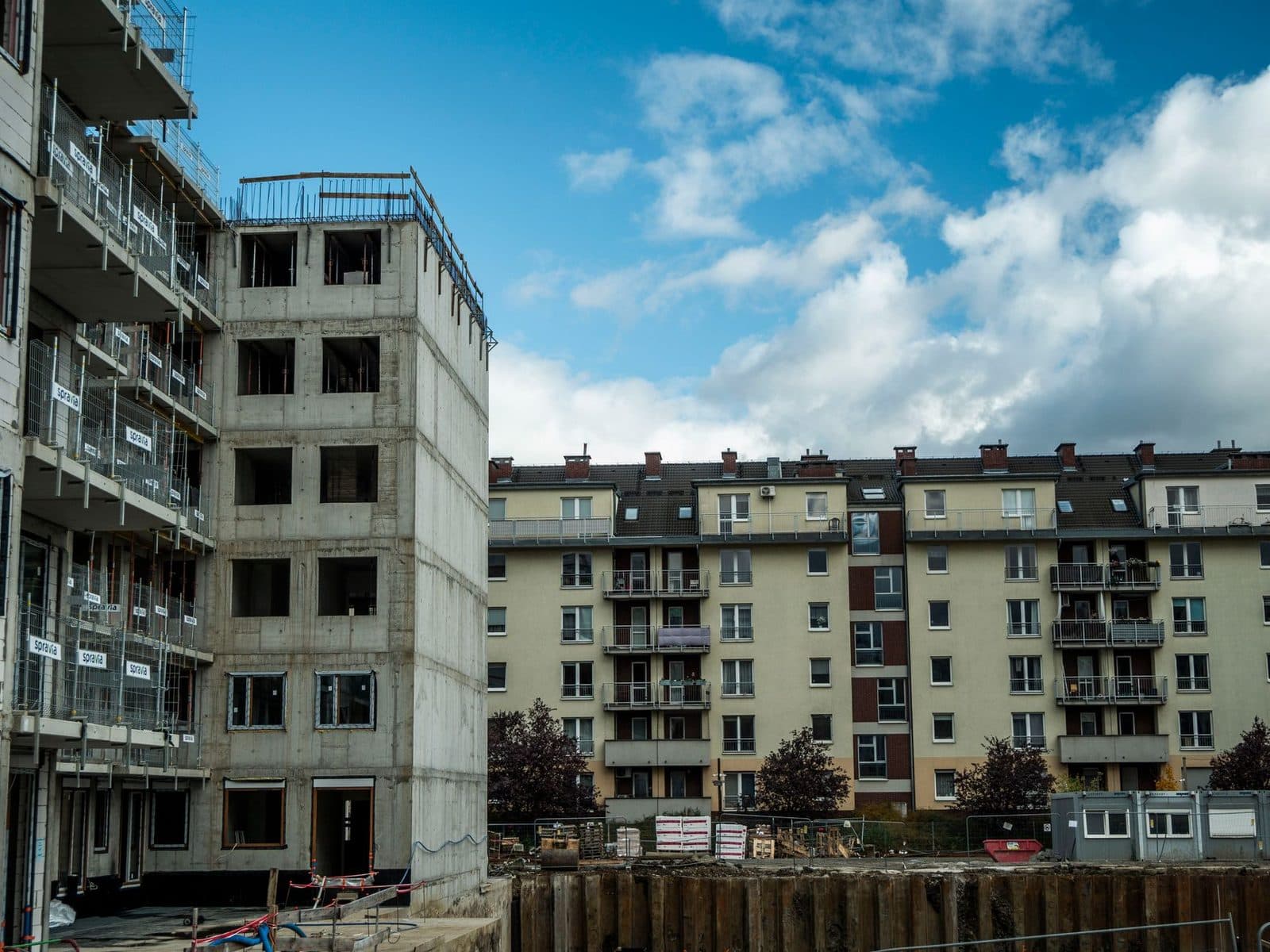 Chantier de construction d'un immeuble en béton avec échafaudages, à côté d'un bâtiment résidentiel existant