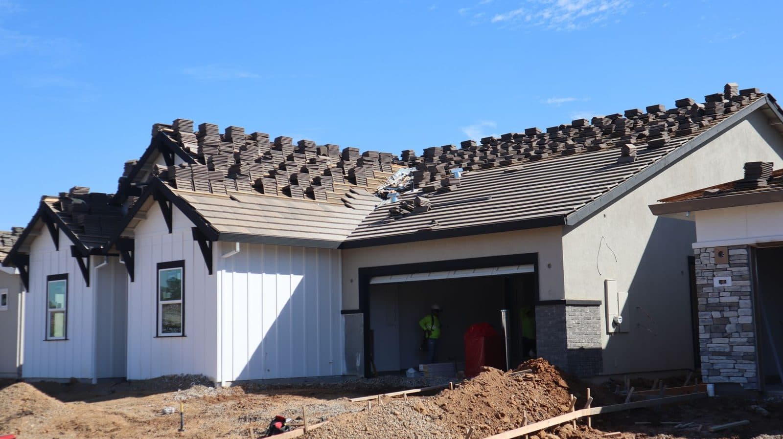 Maison individuelle en construction avec tuiles empilées sur le toit et ouvriers sur le chantier