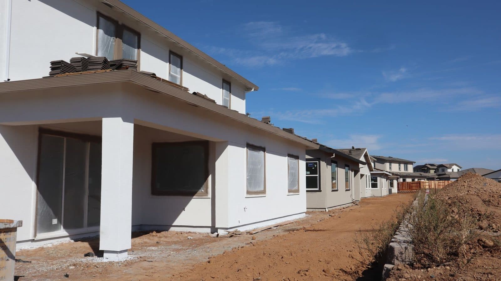 Maisons neuves en construction avec façades enduites, fenêtres protégées et terrain de terre nue