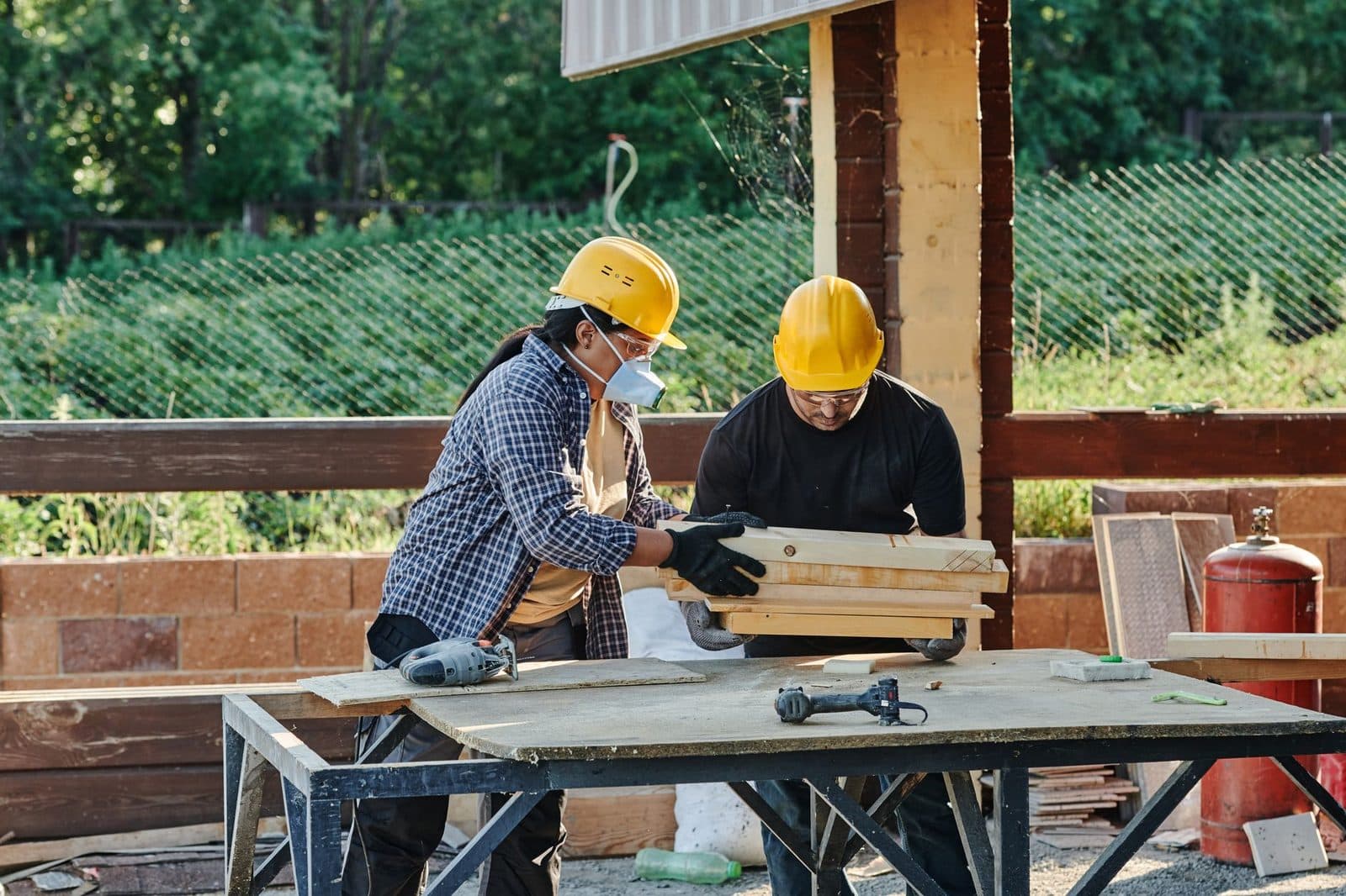 Deux ouvriers en casque jaune manipulant des planches de bois sur un établi d'un chantier de construction
