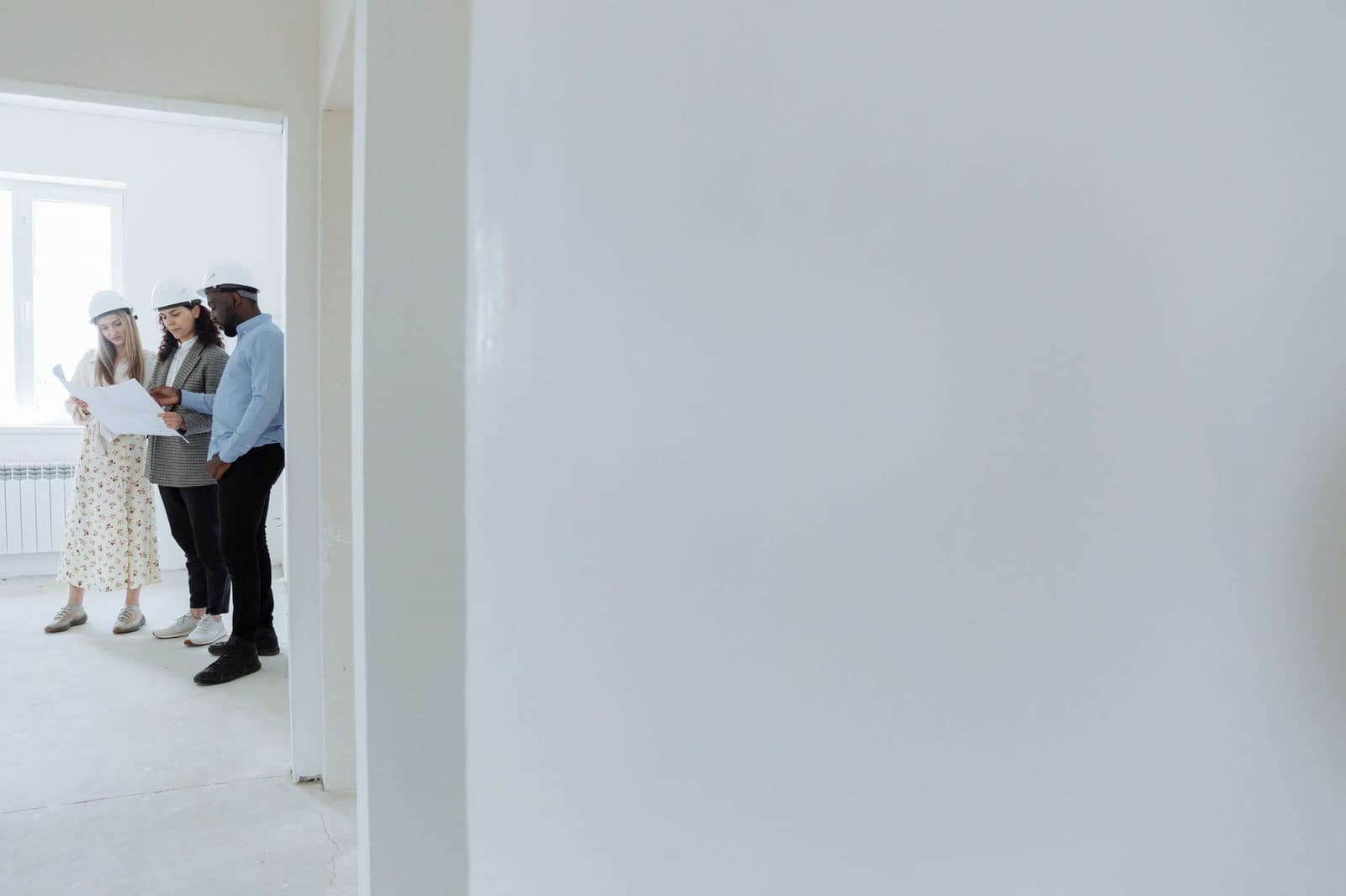 Trois personnes avec casques de chantier examinent un plan dans une pièce vide en cours de rénovation