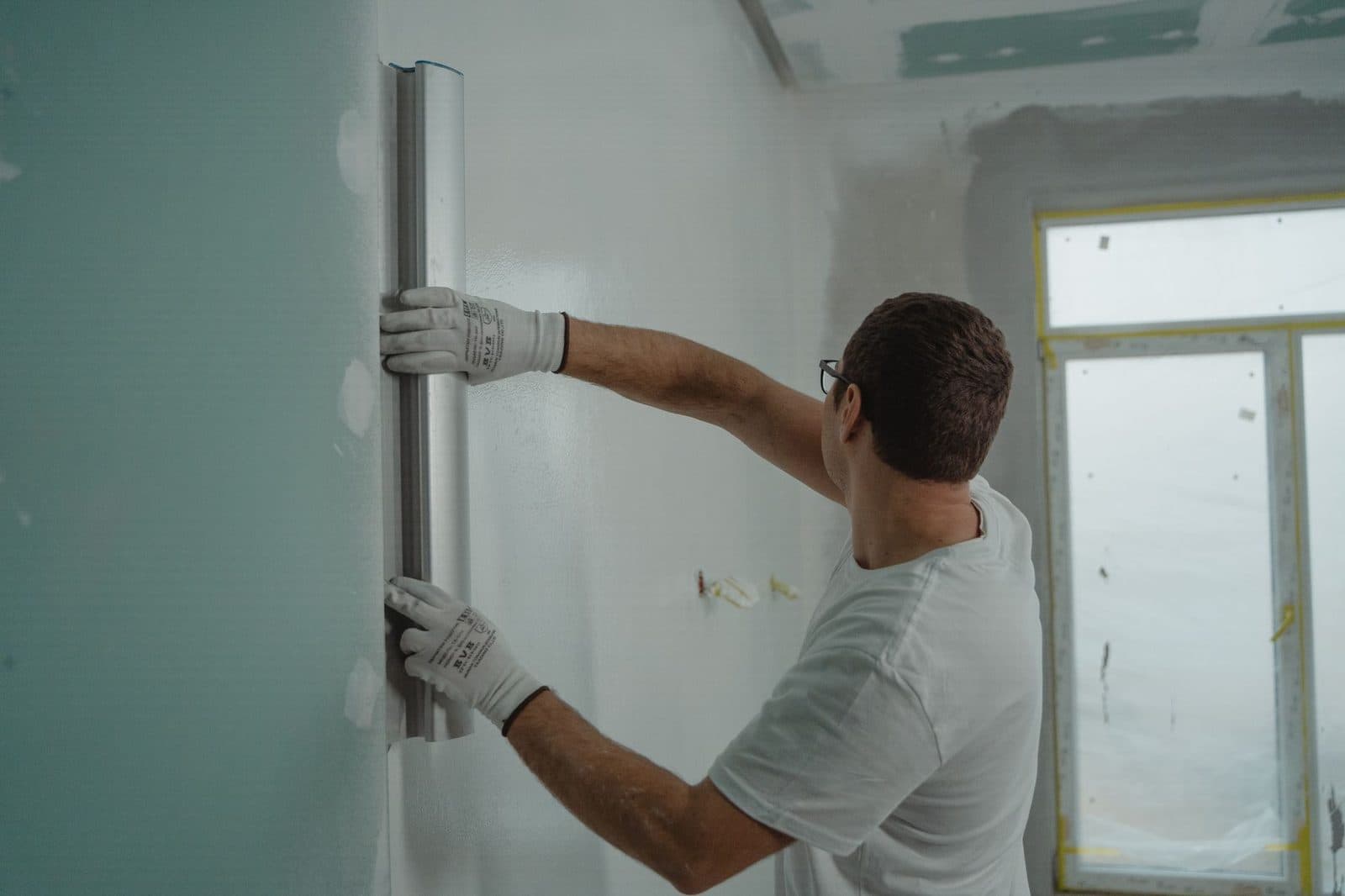 Artisan ganté posant une cornière sur une cloison en plaques de plâtre dans une pièce en rénovation