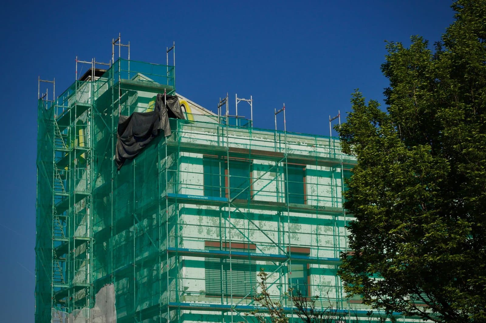 Immeuble en rénovation entouré d'échafaudages et de filets verts, façade en cours d'isolation extérieure