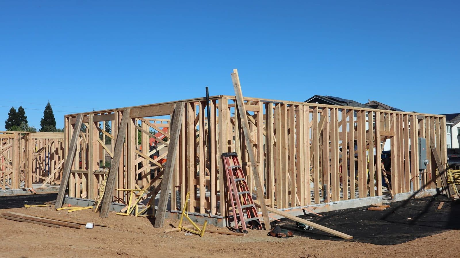 Chantier de construction d'une maison à ossature bois avec échelle et planches, sous un ciel bleu