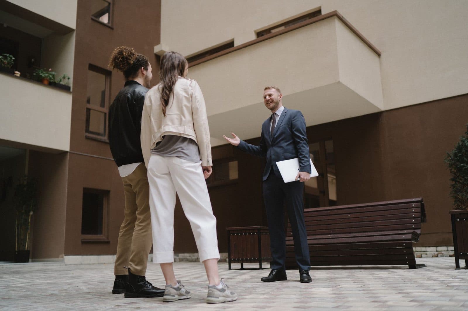 Un homme en costume avec un dossier discute avec un couple dans la cour d'un immeuble résidentiel