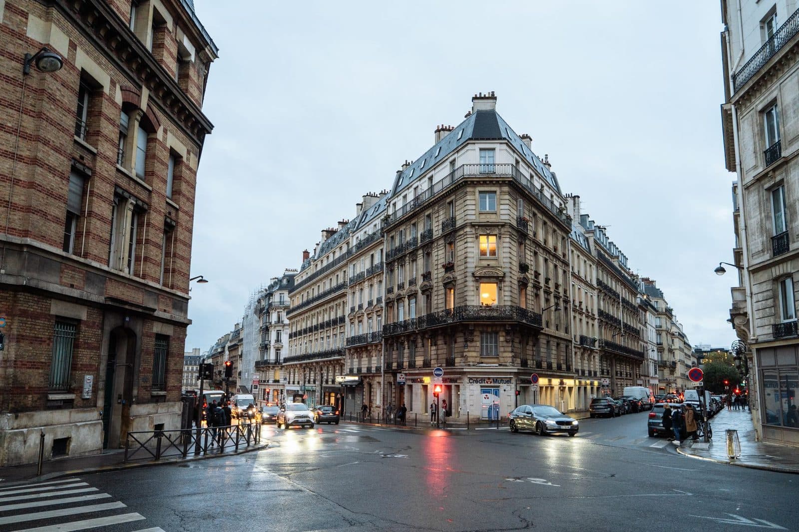 Immeuble haussmannien d'angle à Paris, rue mouillée, voitures et feux rouges au crépuscule