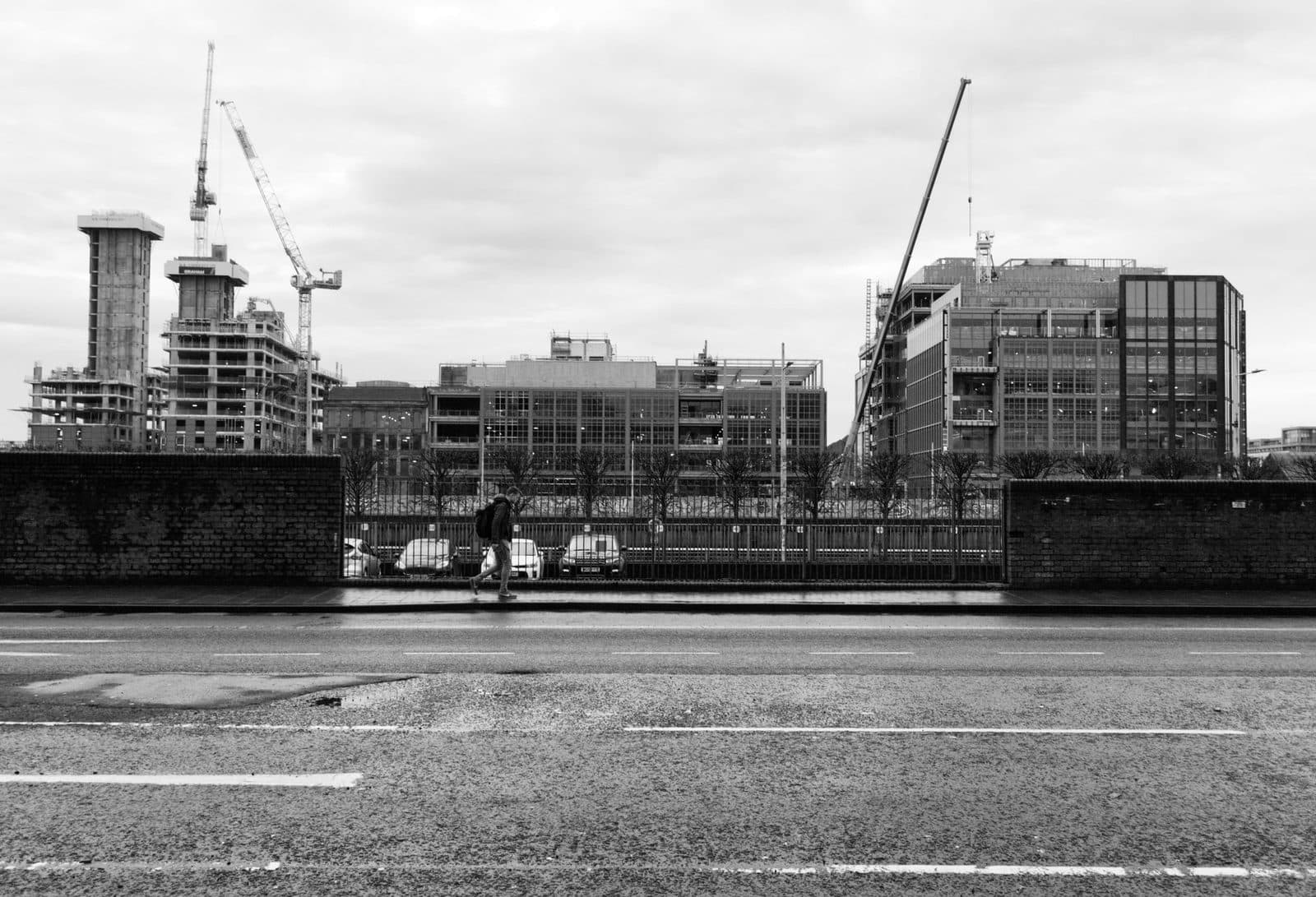 Photo en noir et blanc d'un chantier urbain avec grues, immeubles en construction et passant le long d'une route