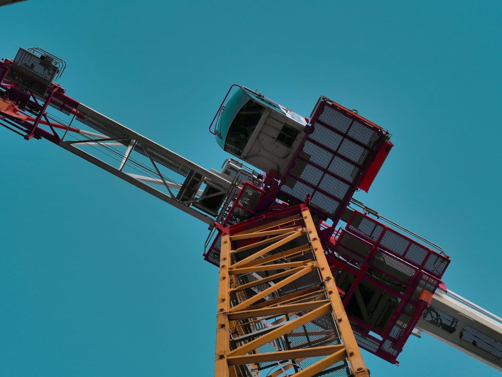 Vue en contre-plongée d'une grue de chantier jaune et rouge avec sa cabine, sur fond de ciel bleu