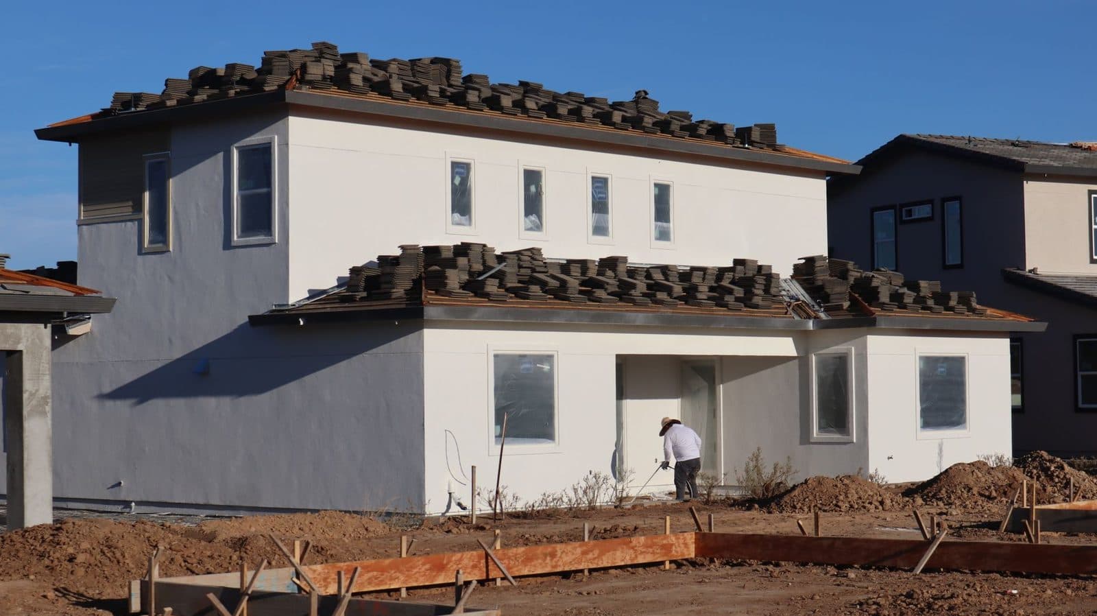 Maison neuve en construction avec tuiles empilées sur le toit et ouvrier sur le chantier