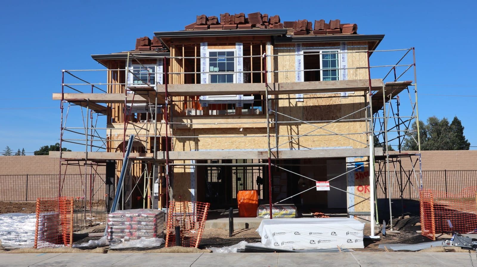 Maison résidentielle en construction à ossature bois entourée d'échafaudages, sous un ciel bleu