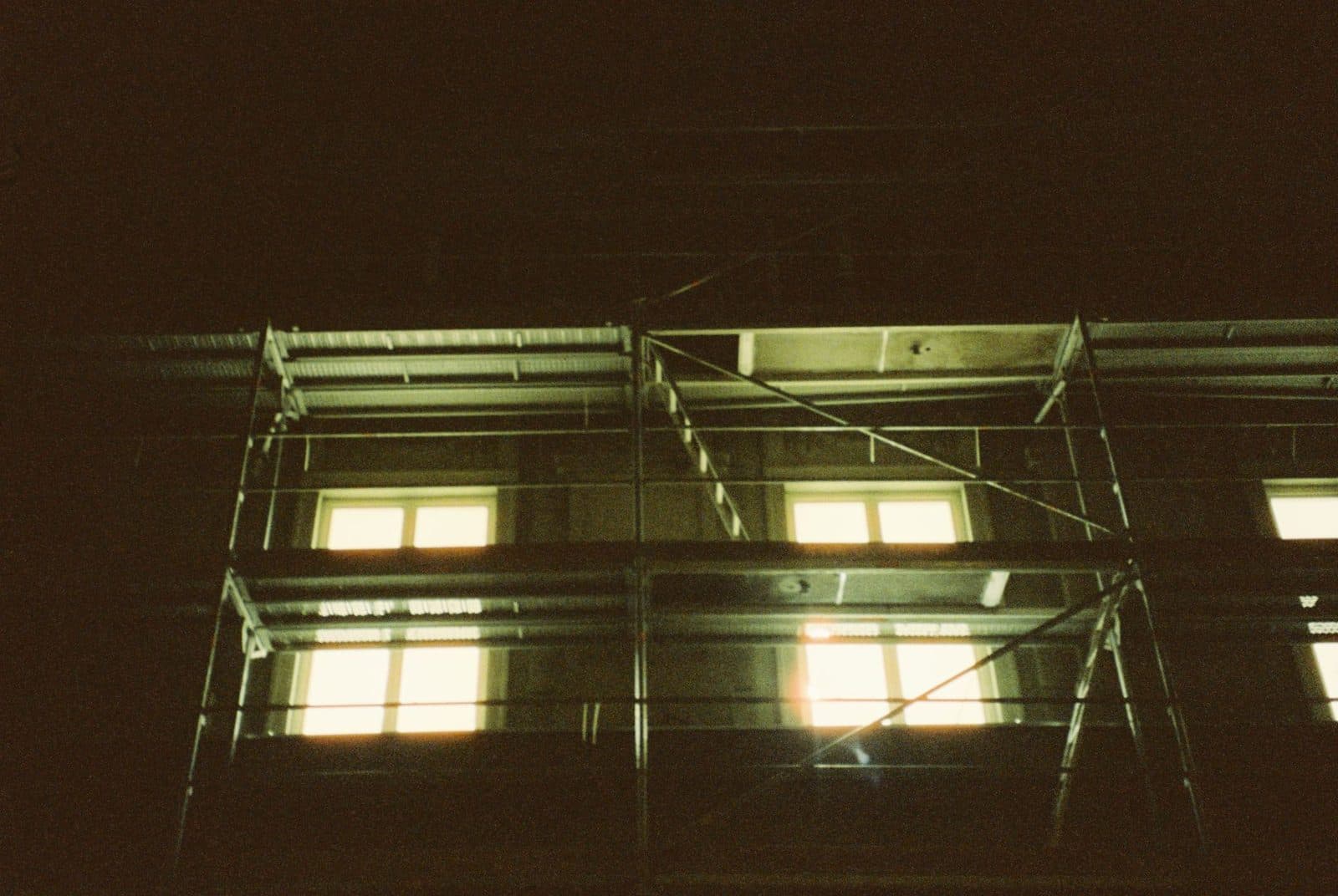 Échafaudage installé de nuit devant la façade d'un immeuble en travaux, fenêtres éclairées