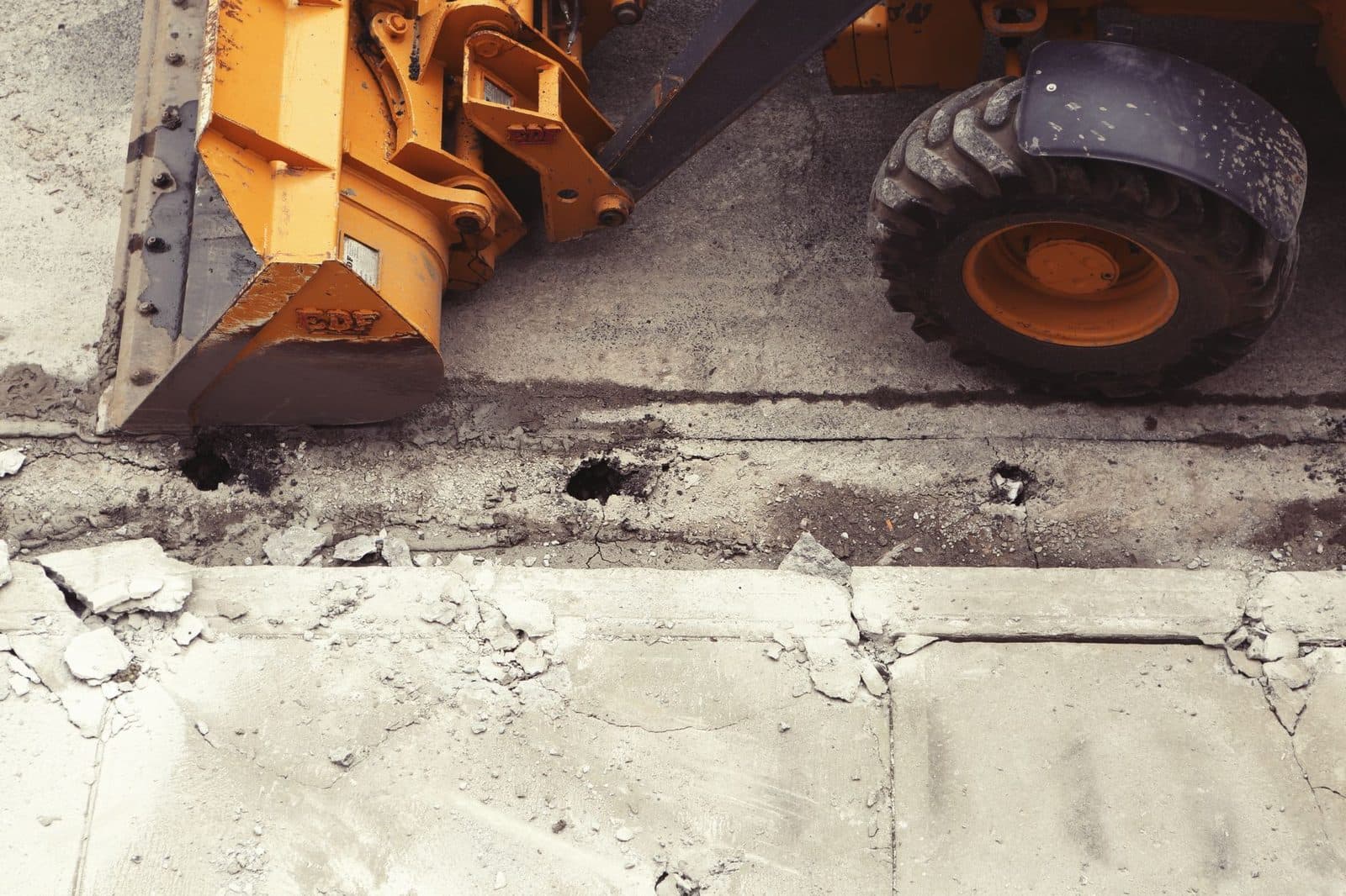 Chargeuse jaune démolissant une dalle de béton, gravats et débris sur un chantier