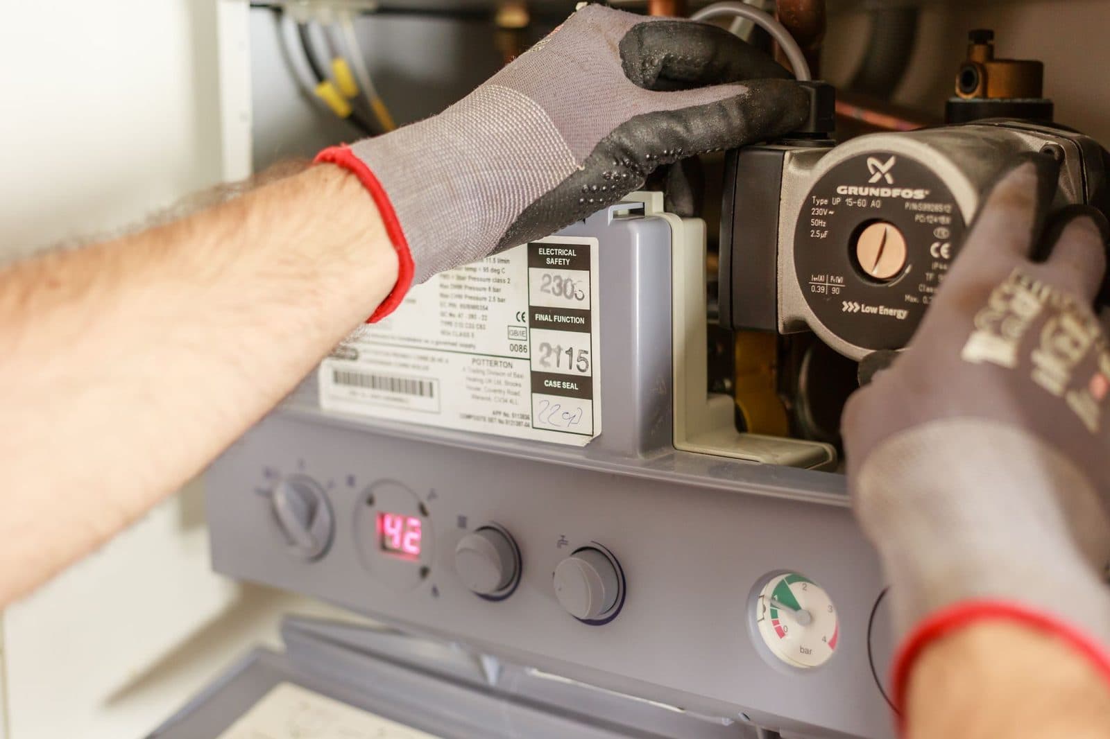 Gros plan des mains gantées d'un technicien travaillant sur une chaudière à gaz.
