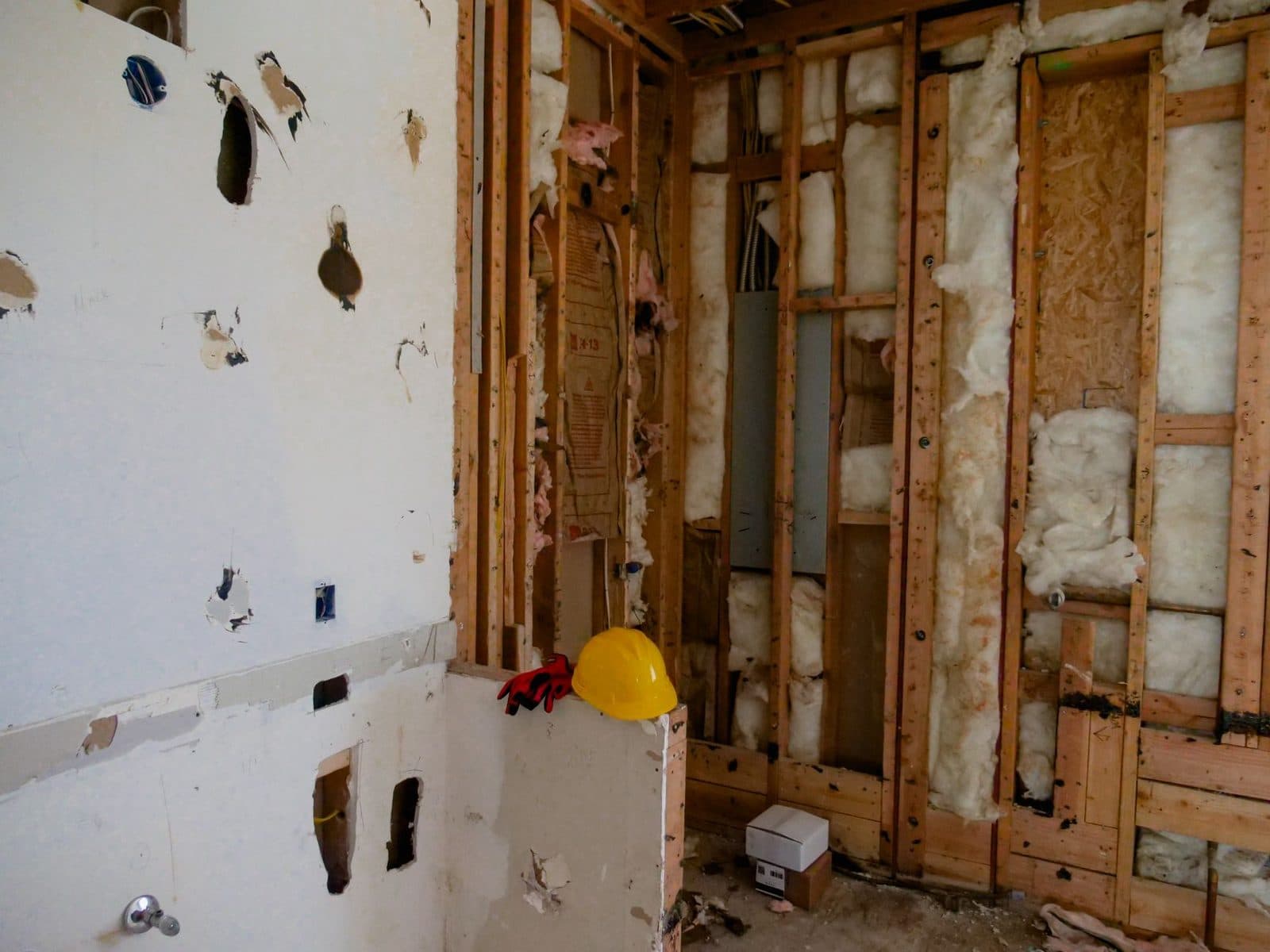 Chantier de rénovation : murs ouverts, isolation en laine minérale entre montants de bois, casque jaune