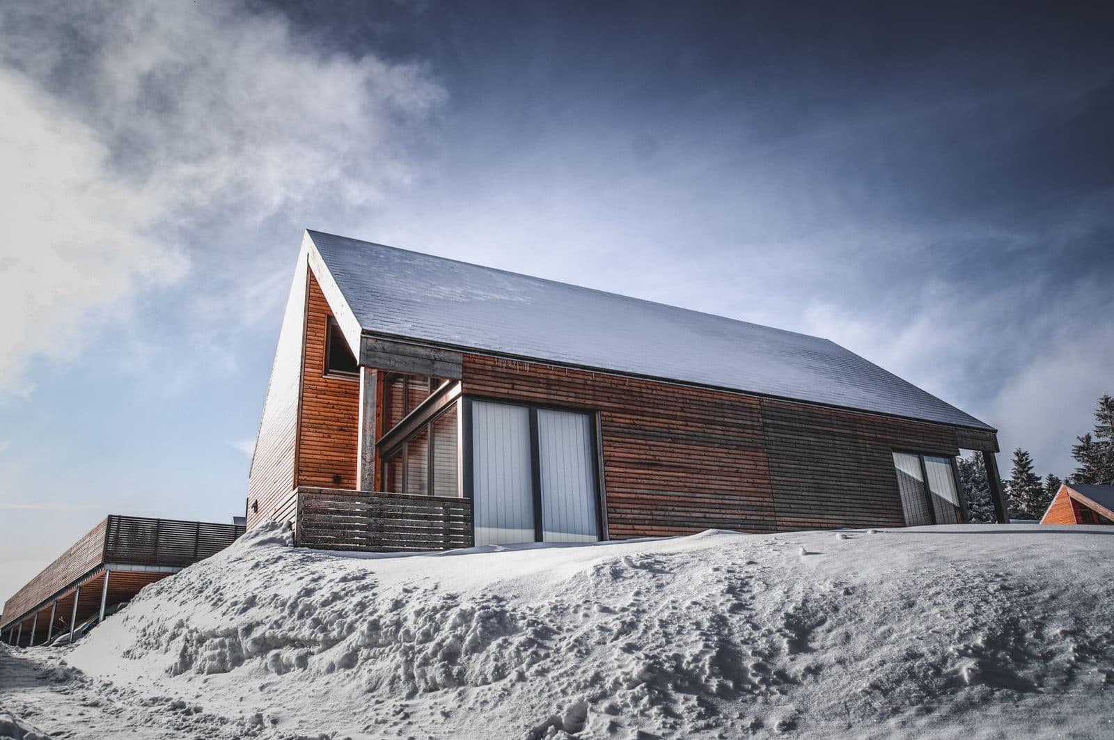 Maison contemporaine à bardage bois et toiture sombre sur une colline enneigée, sous un ciel bleu