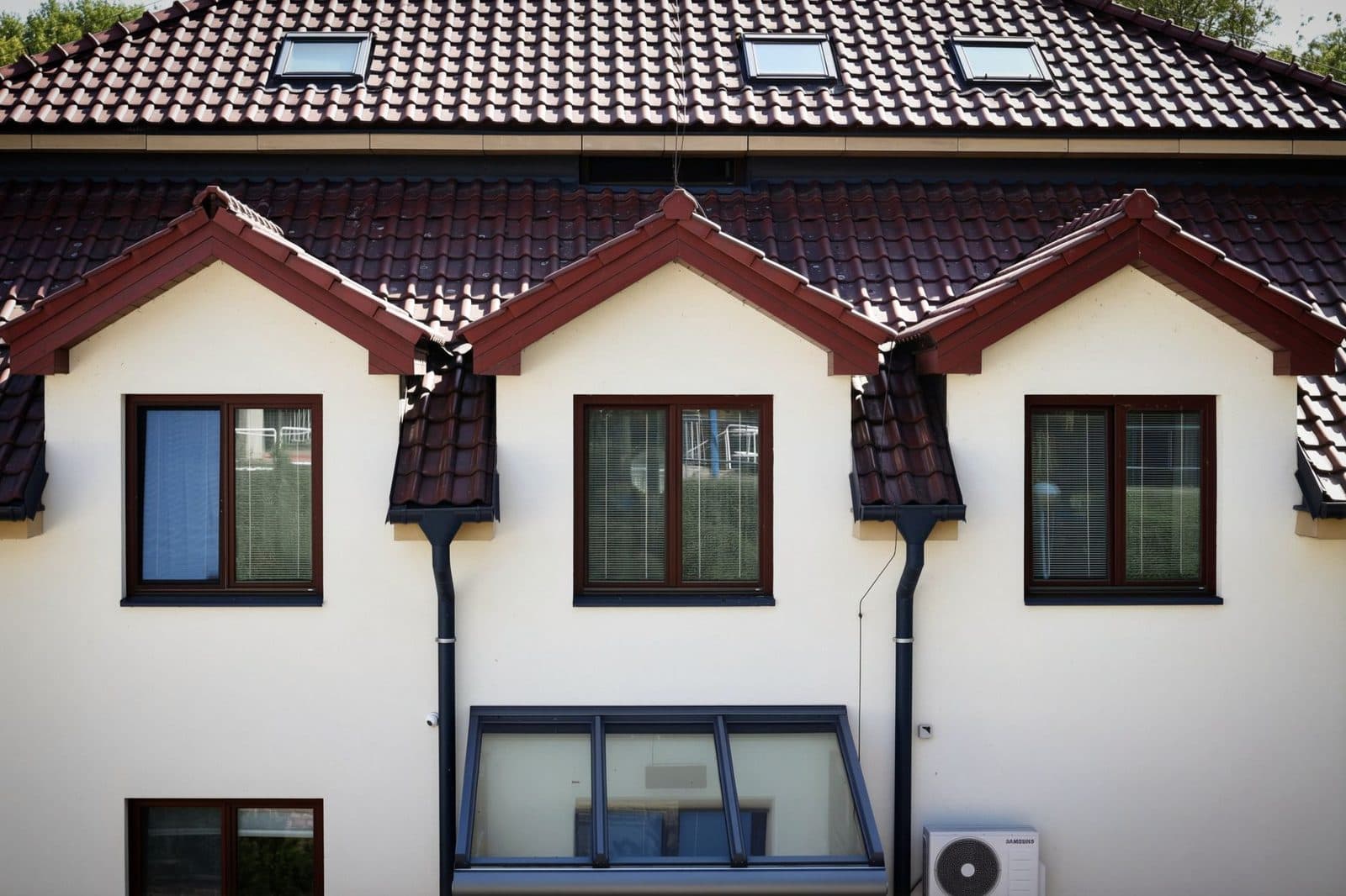Façade de maison avec toiture en tuiles, fenêtres de toit, lucarnes et unité extérieure de pompe à chaleur