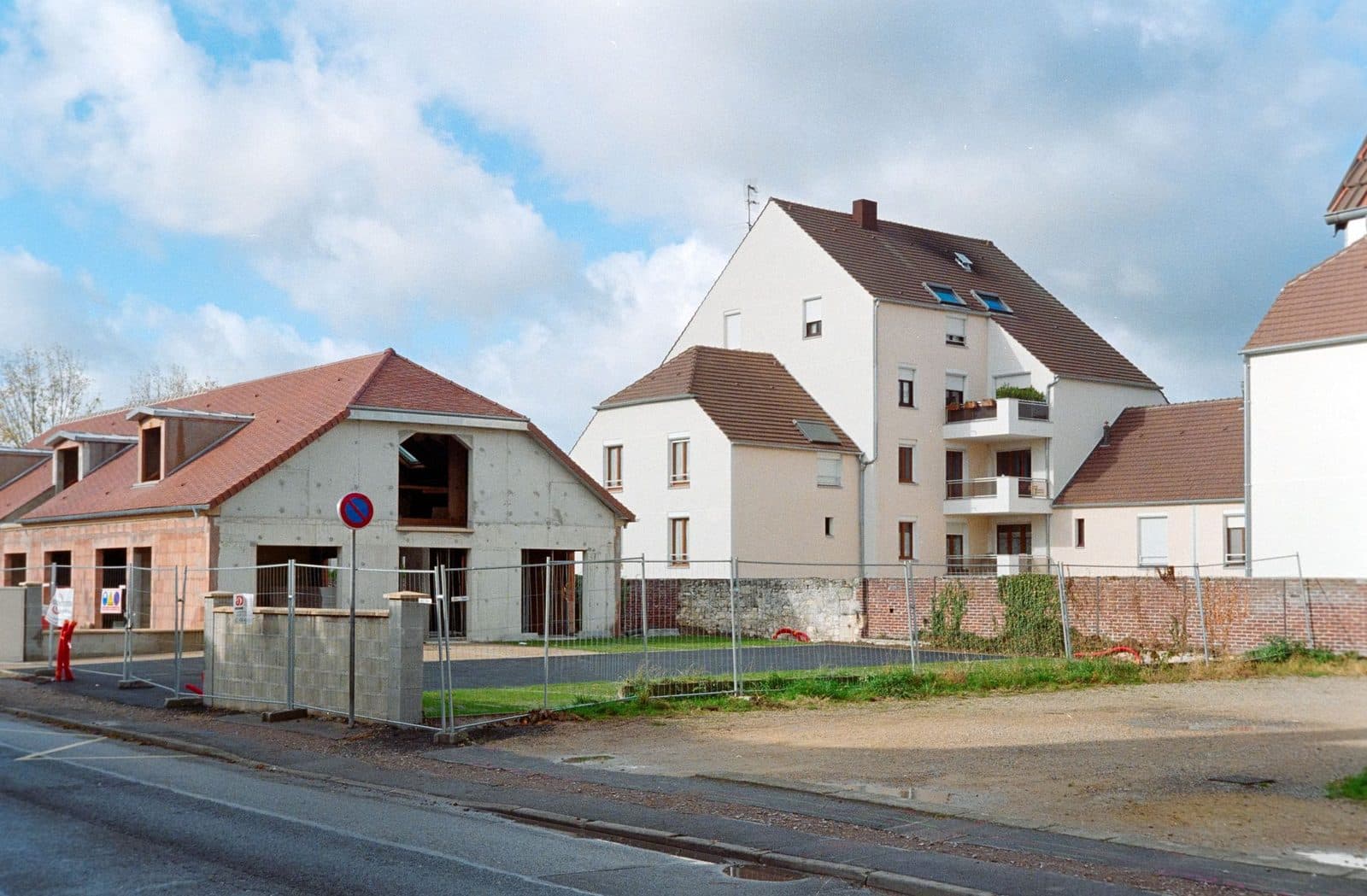 Chantier de construction clôturé avec maison en parpaings en cours d'édification devant des immeubles résidentiels
