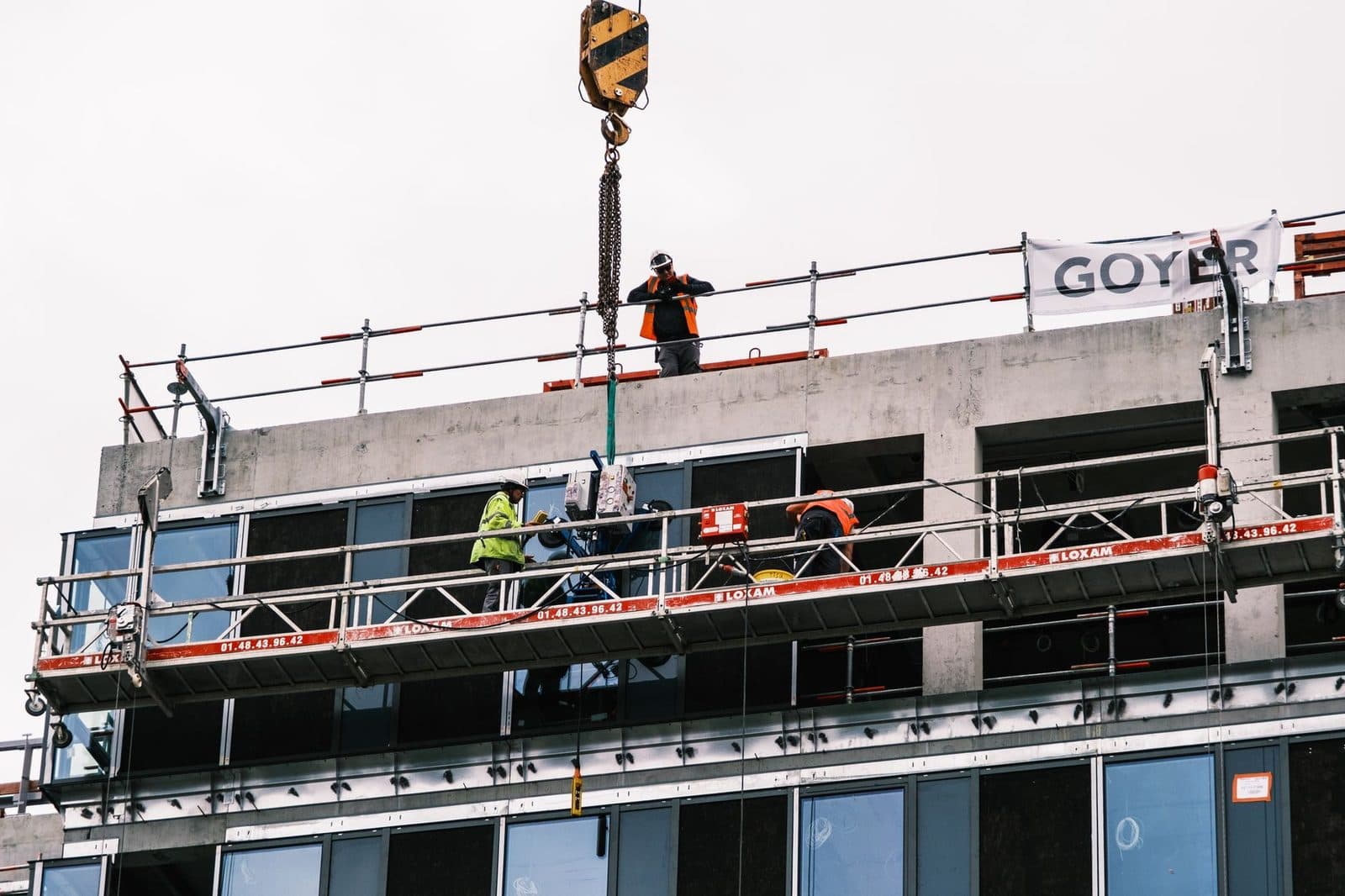 Ouvriers sur une nacelle suspendue posant des vitrages en façade d'un immeuble en chantier, grue en action