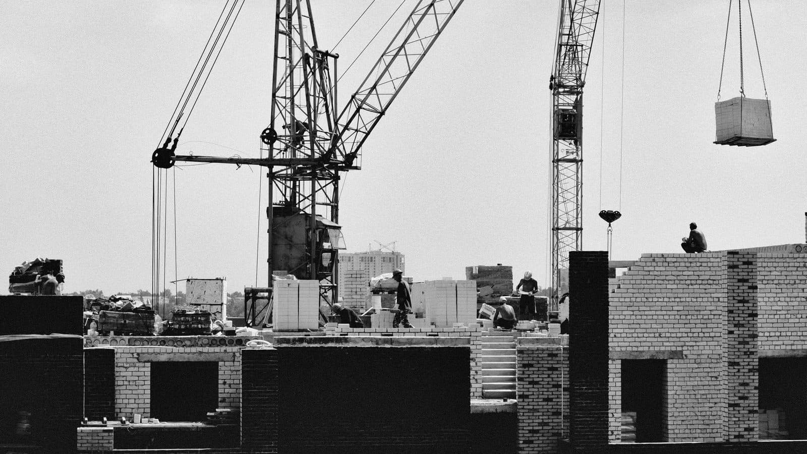 Chantier de construction en noir et blanc avec grues, ouvriers et murs de briques en cours d'élévation